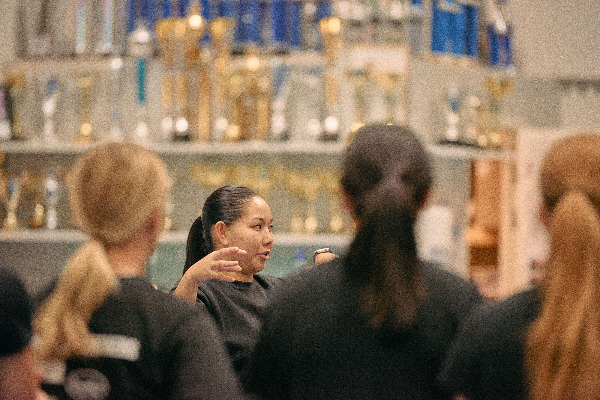 En kvinna med svart  hår uppsatt i en tofs pratar engagerat till ett gäng ungdomar som ska påbörja sin träning.
