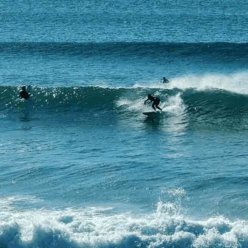 Surfers ride waves on sunny day – surfboard rental in sines