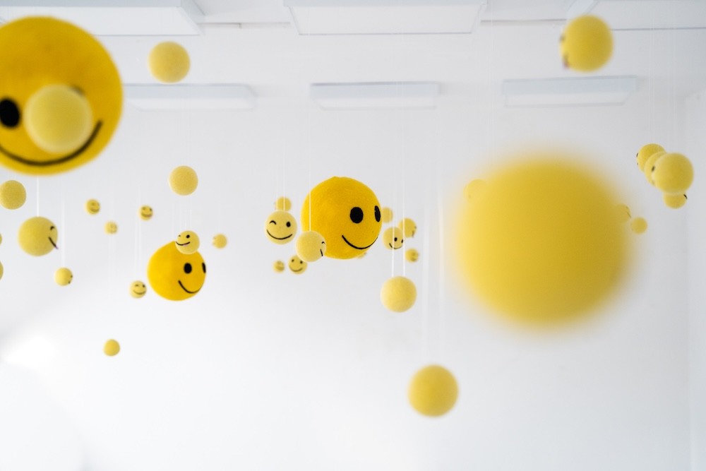 Žlté smiley objekty z vlny visiace v bielom galériovom priestore – dielo Niny A. Šoškovej