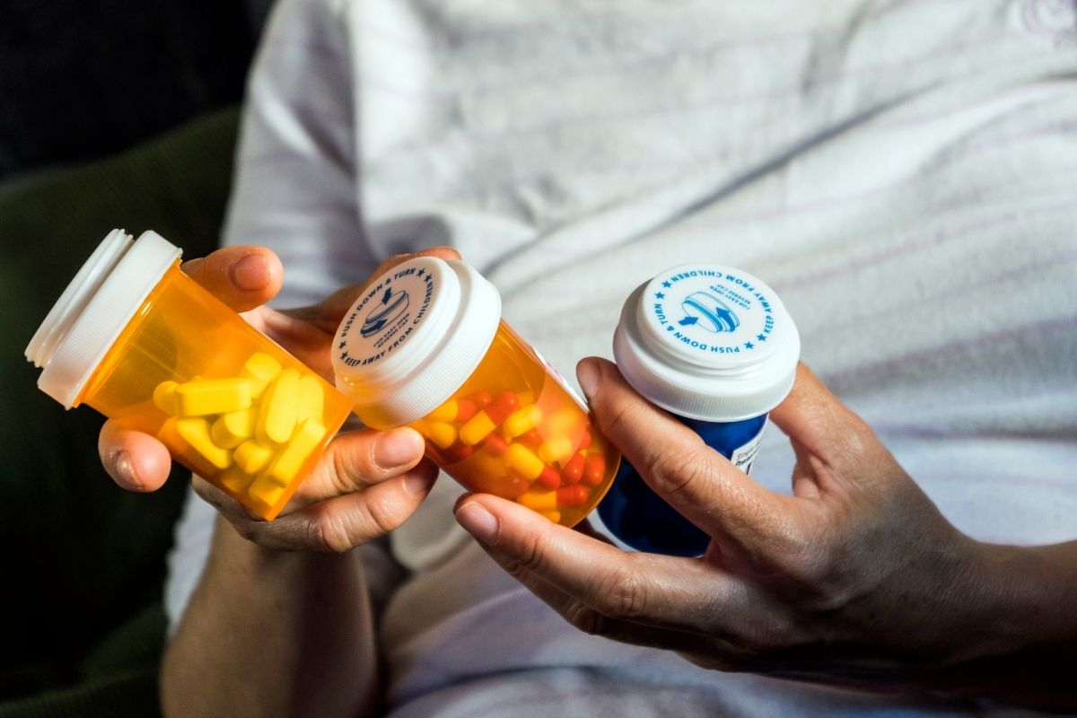 Elderly person holding three different prescription bottles.