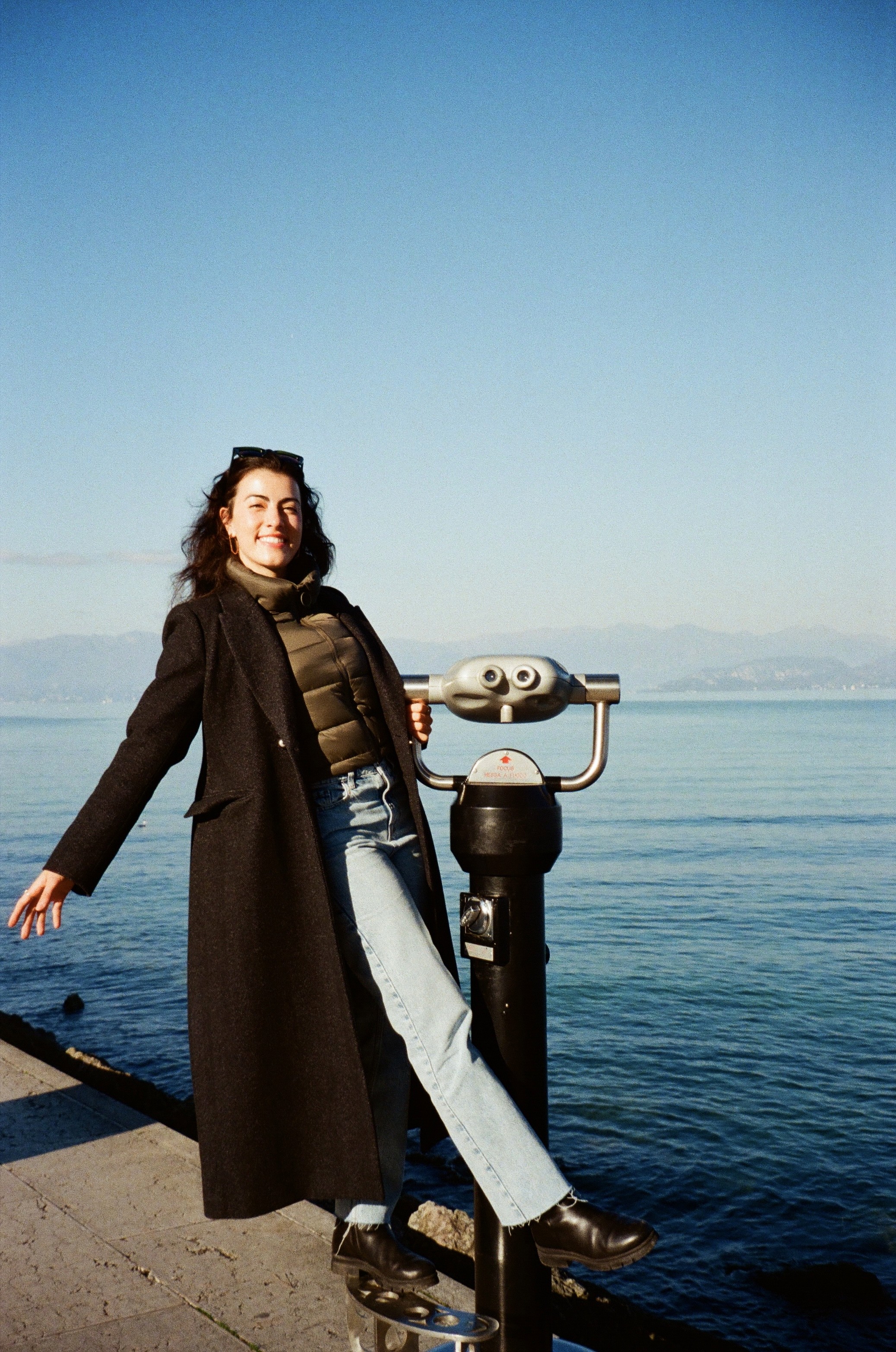 A view from an airplane window shows the aircraft's wing with a golden hue reflecting the setting sun, against a serene backdrop of fluffy clouds and a clear sky.