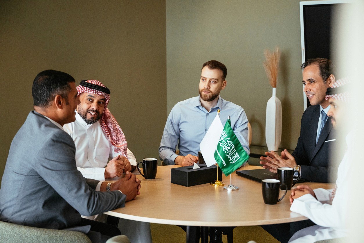 Four professionals seated around a table, engaged in discussion with drinks and notes in an office setting.