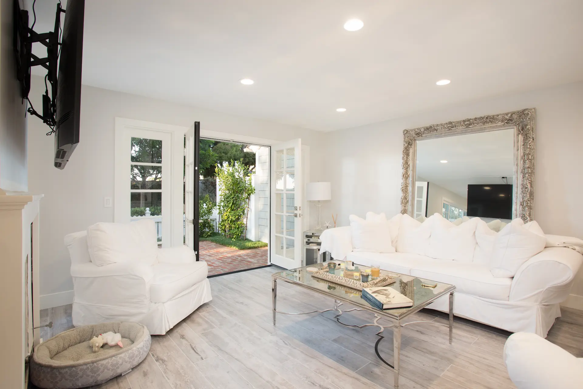 Elegant living room with white couches, gray hardwood floors and decorative mirror. From Dana Point Cape Cod remodel. Photo by Chris Darnall.