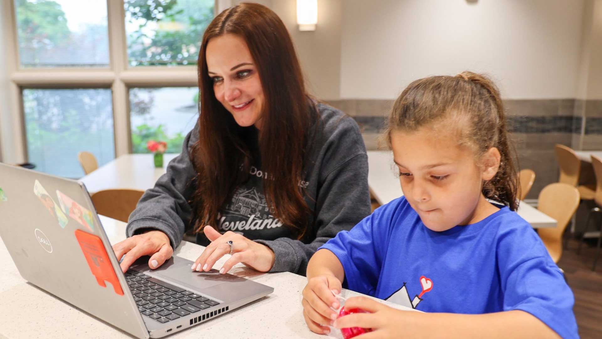 Mom using computer at kitchen counter sitting next to her daughter