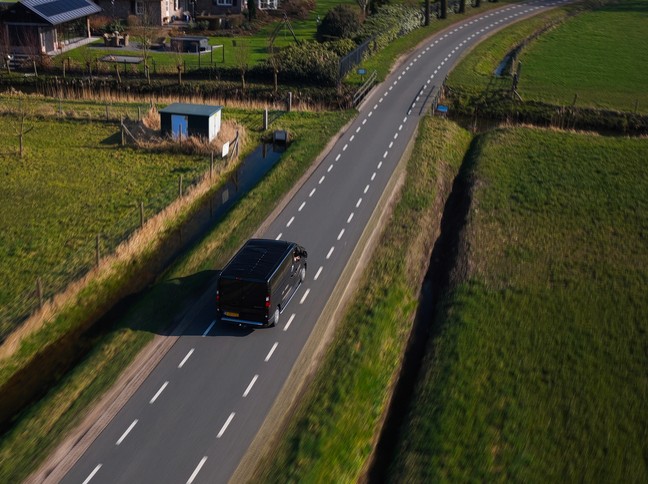 Luchtfoto van een zwarte Van Ede Koeriers bus rijdend op een polderweg in de buurt van Utrecht.