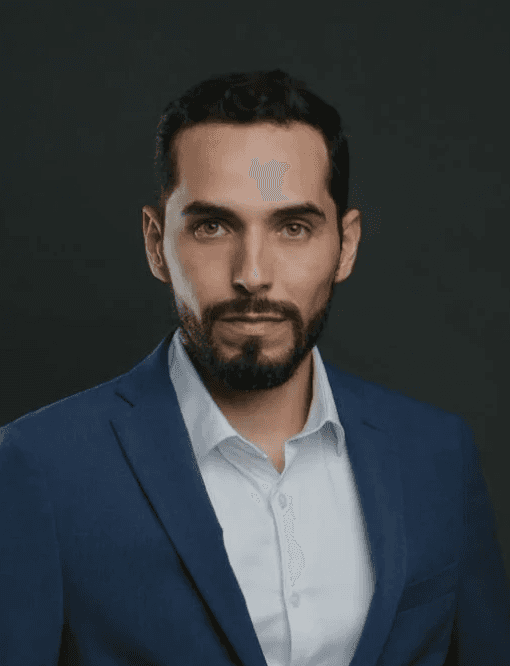 man in blue dress shirt and black pants standing near white wall