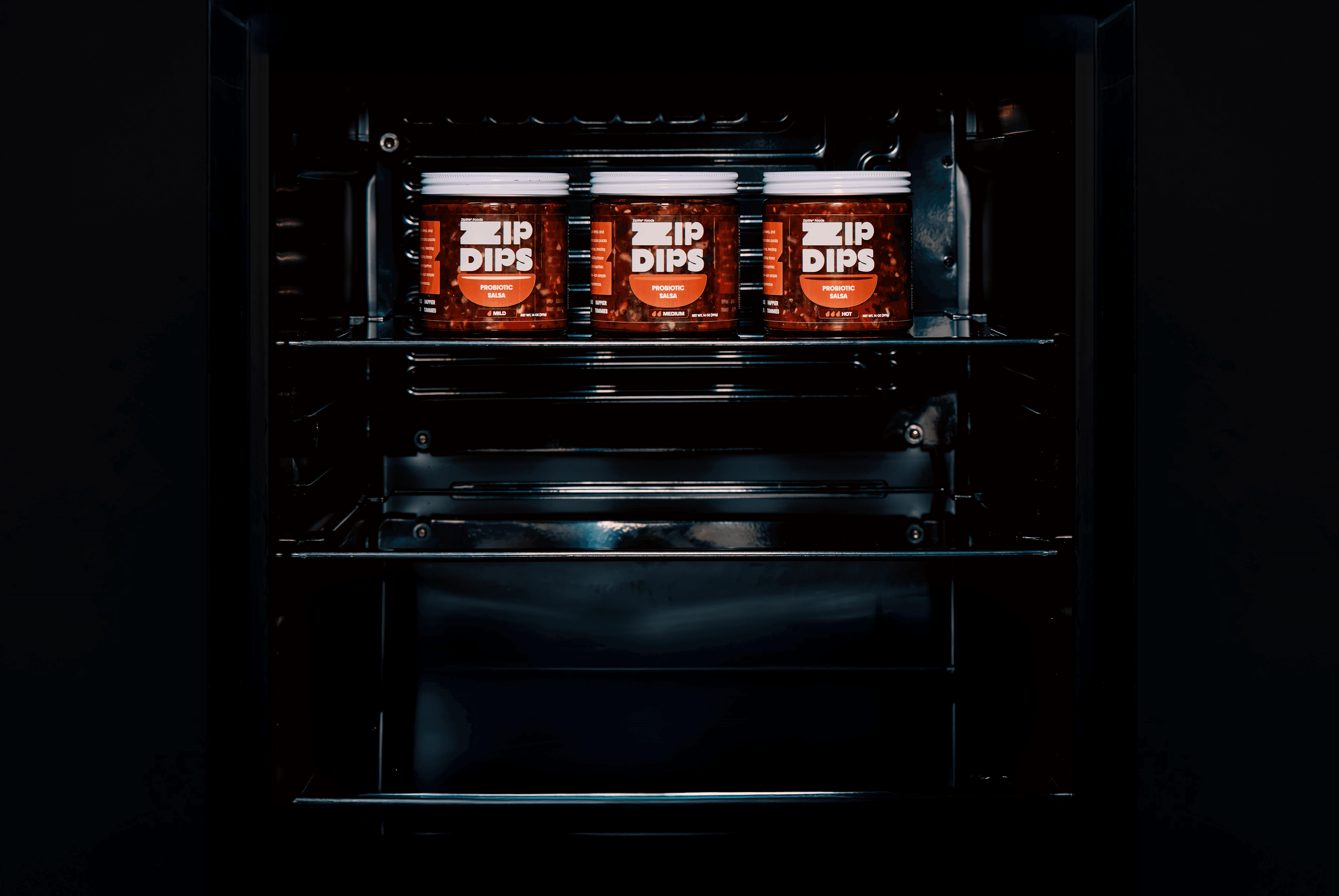 A dark shelf features three red glass bottles arranged neatly in a compact display. On the bottle it says the flavor mild medium hot