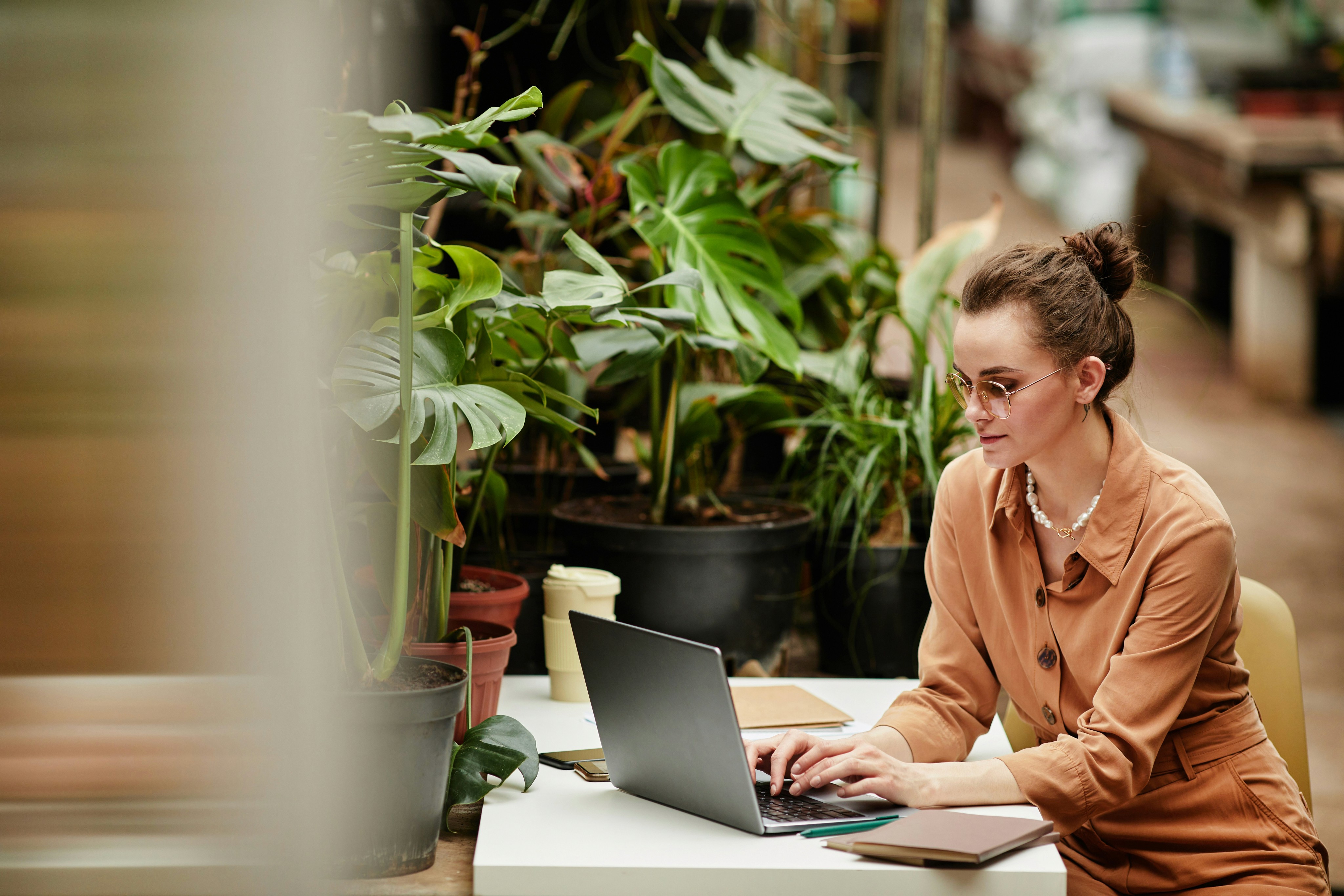 woman in an orange business shirt on her computer surrounded by plants