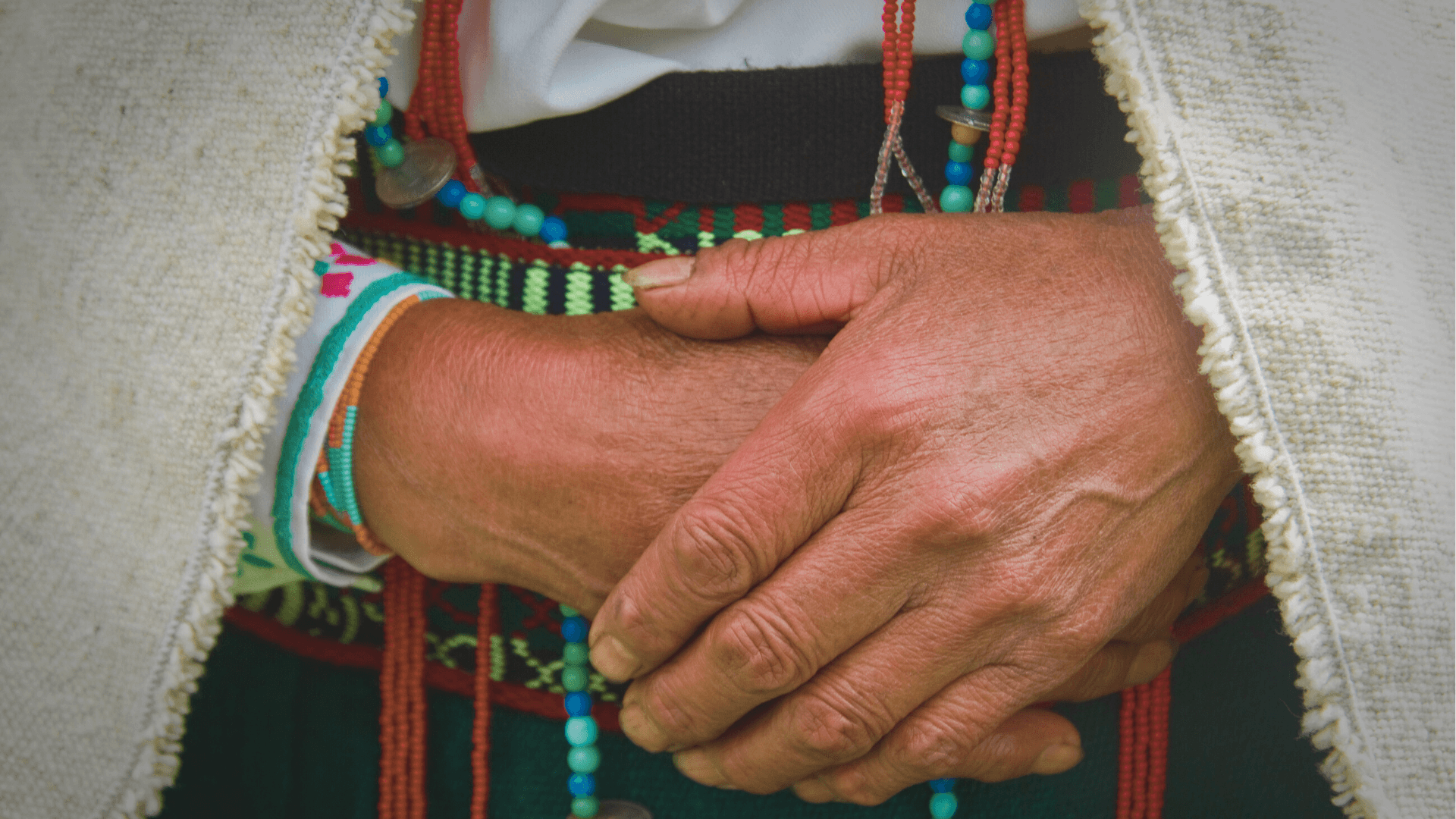 Close-up of hands adorned with colorful bracelets, gently clasped together, showcasing intricate details and textures.