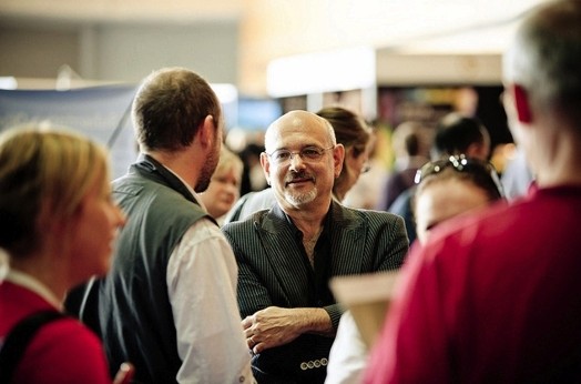 A photo of two people talking while standing among other people.