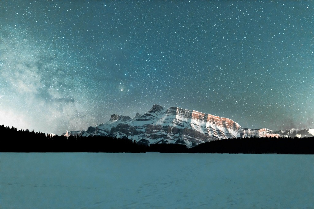 A snow-covered lake with a mountain in the background and stars above