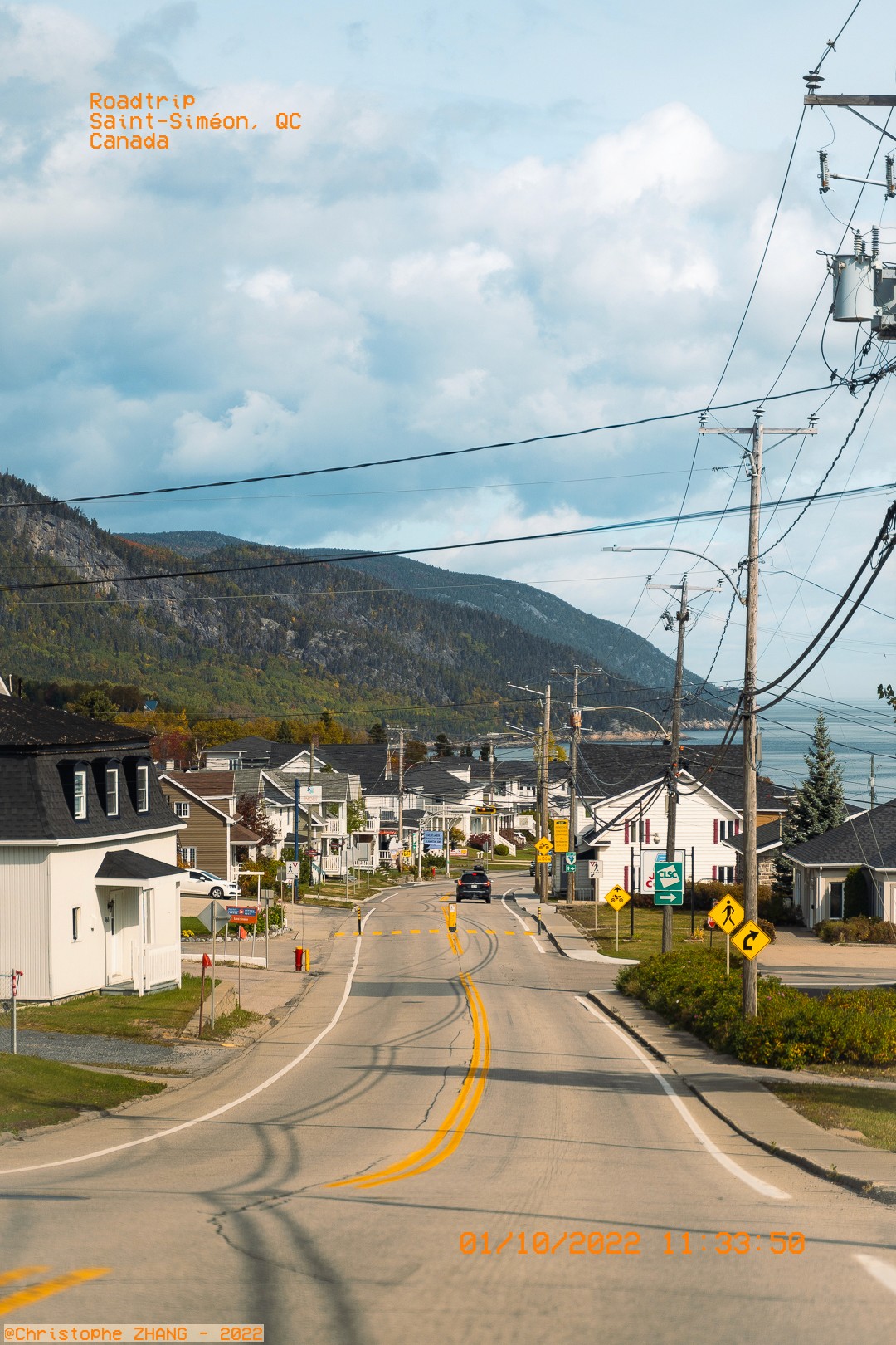 Route de village à Saint-Siméon avec vue sur les montagnes et le fleuve en arrière-plan.