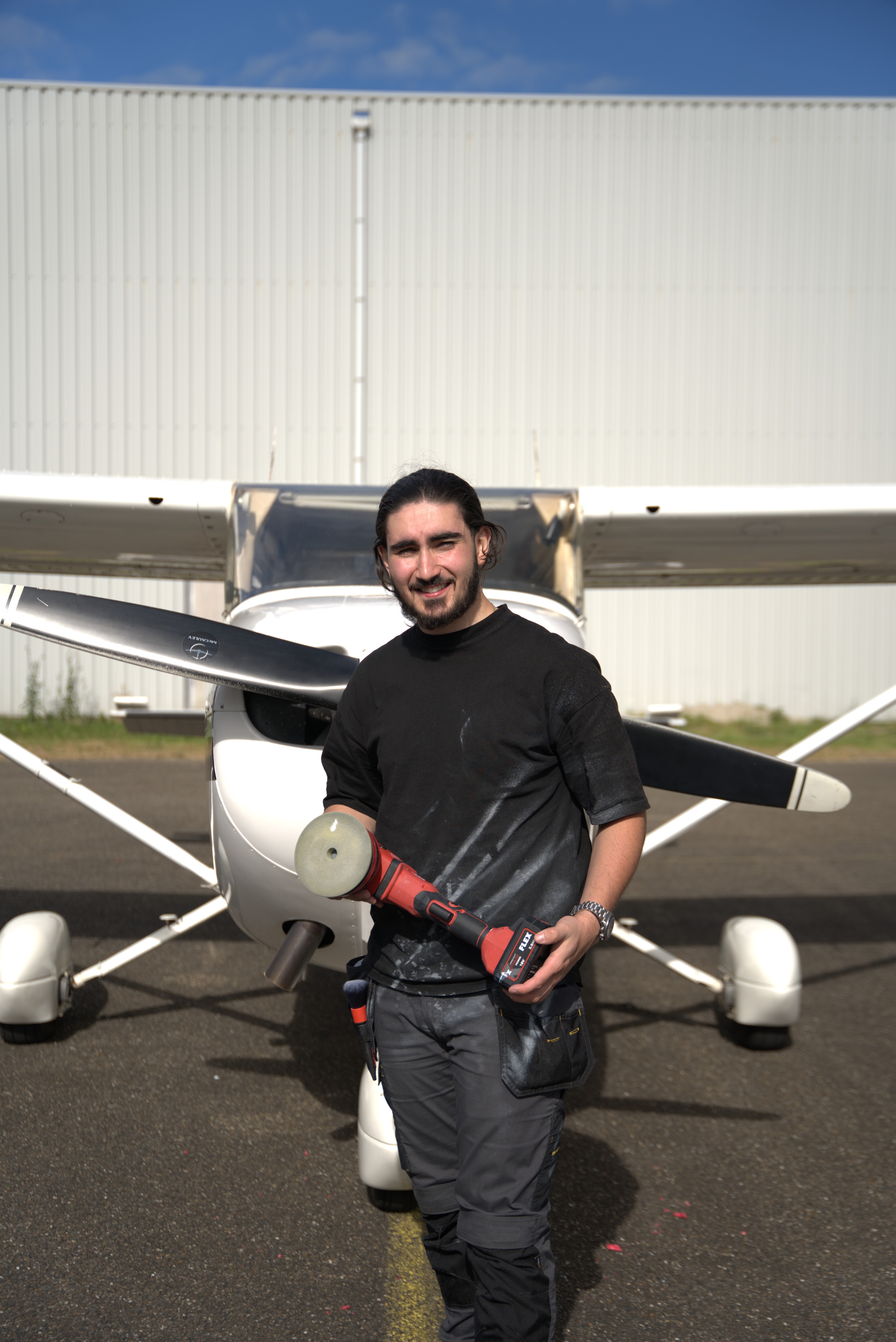 Mikail van Micky’s Cleaning staat met zijn polijstmachine naast een klein vliegtuig, vastberaden om elk voertuig met passie en vakmanschap te laten stralen.