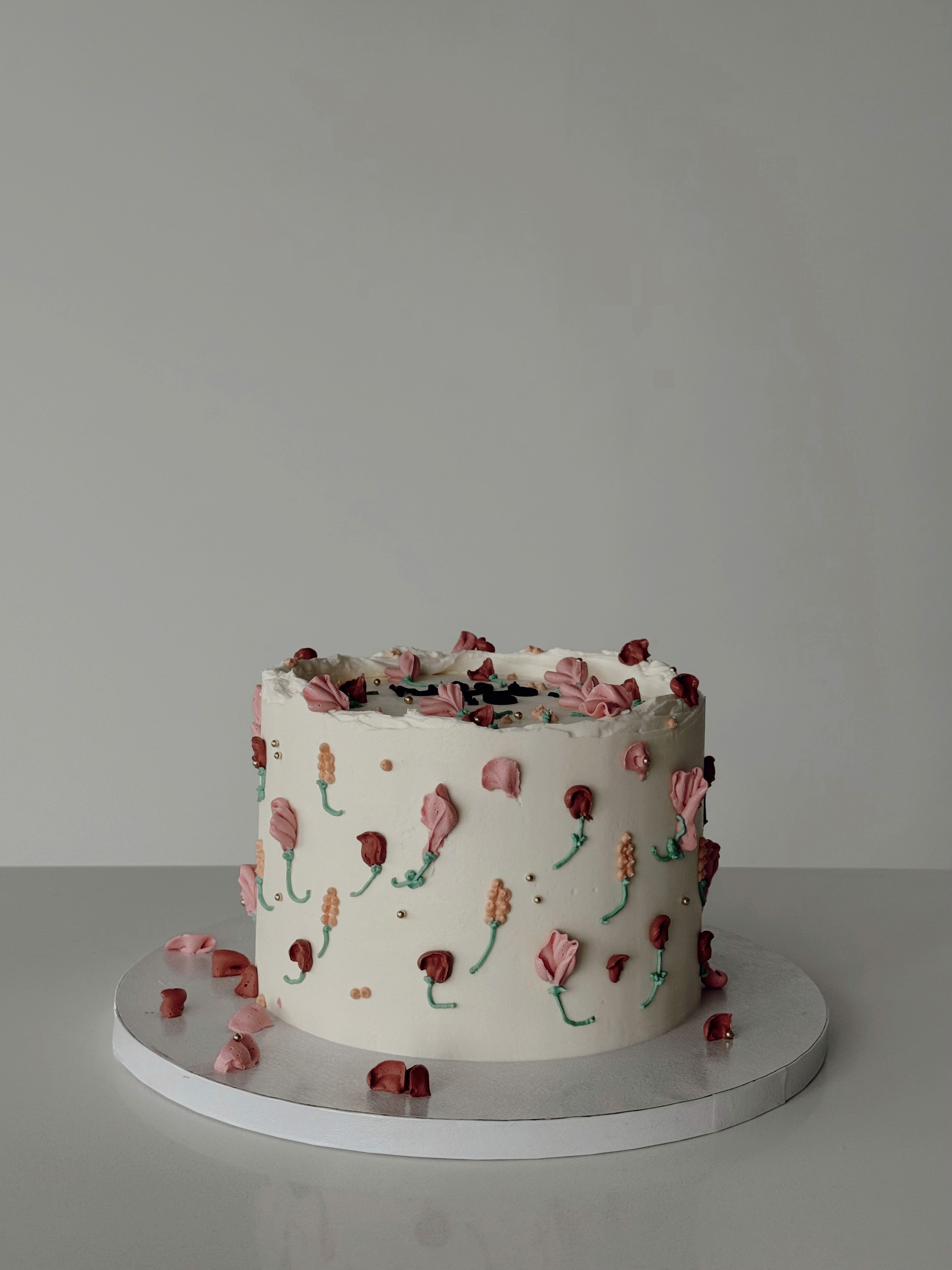 White buttercream cake decorated with pink petals and delicate green stems