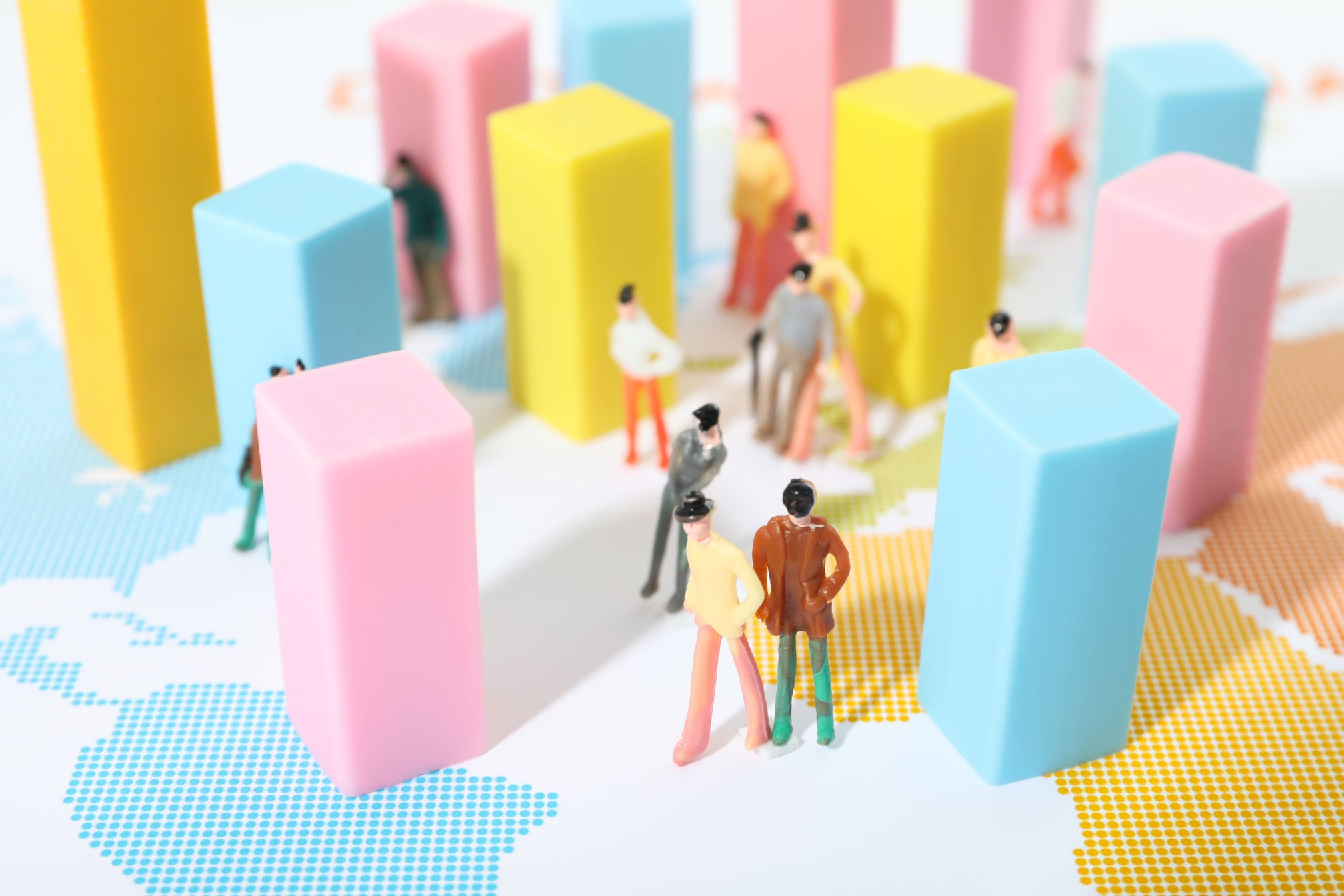 Kolorowe słupki statystyk oraz miniaturowe figurki ludzi rozmieszczone na mapie świata jako ilustracja badań demograficznych i planowania zasięgu kampanii