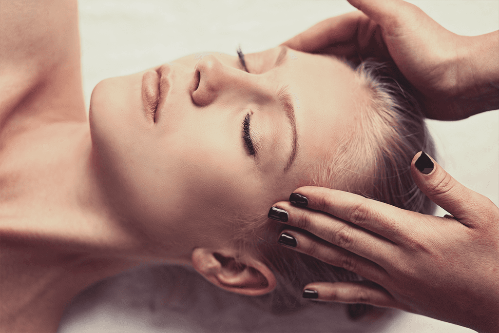 Woman lying on a massage table at home, receiving a calming head massage in a peaceful setting