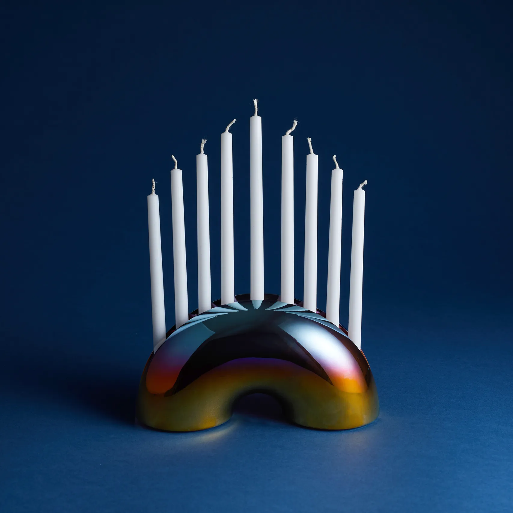 Iridescent Nosh Menorah with white candles on a dark blue background