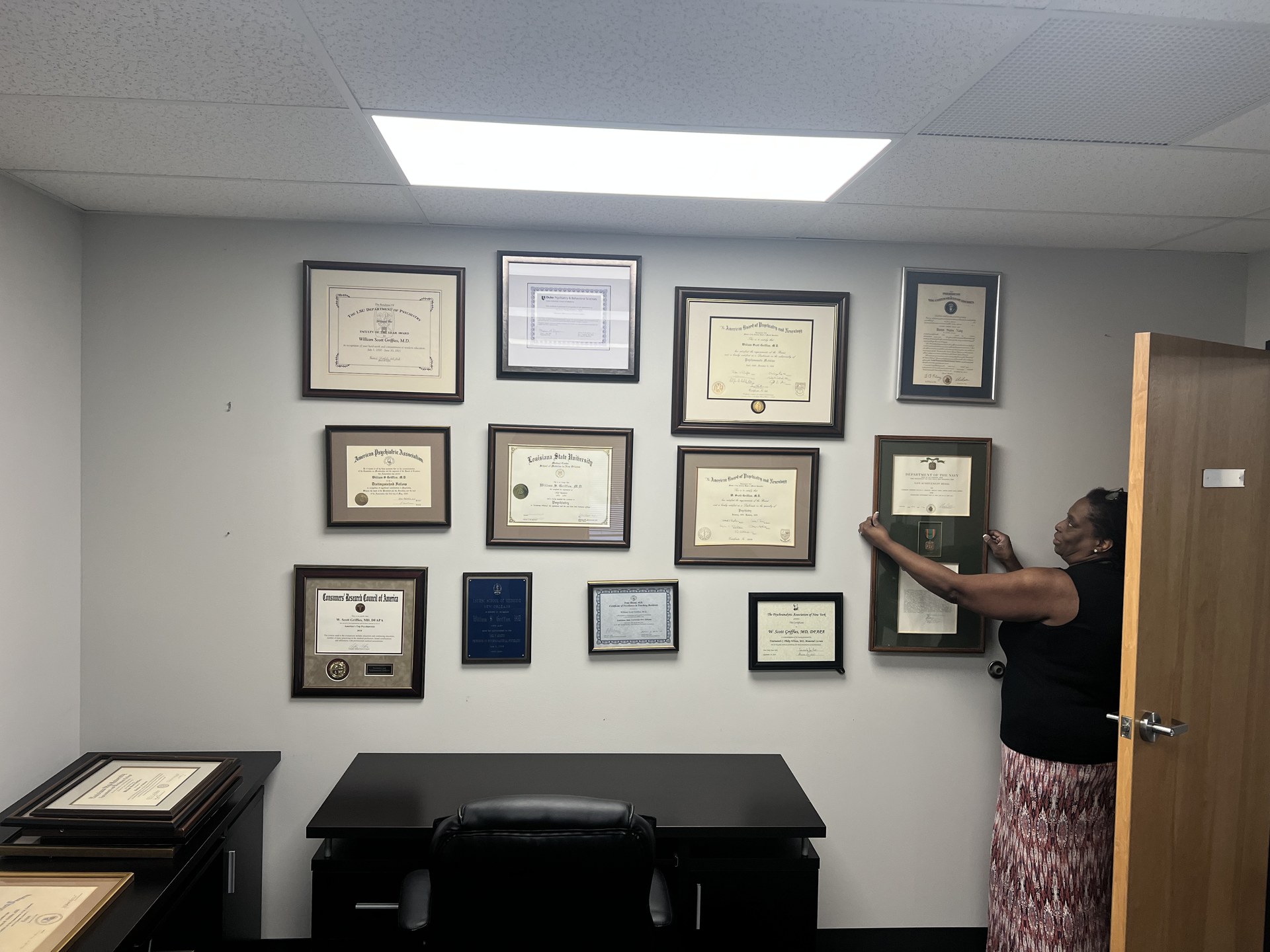 Office staff member indicating the previous framed-credential arrangement.