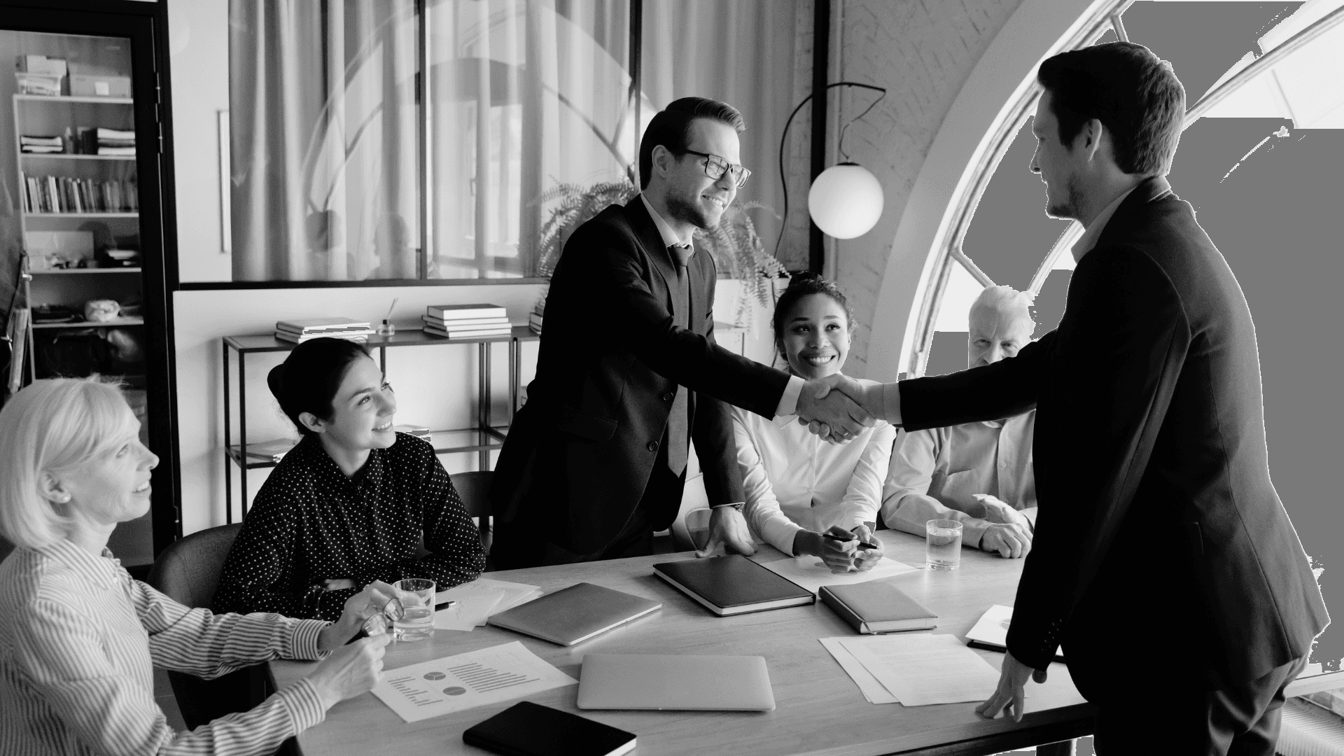 Two colleagues collaborating over paperwork at an office desk, with plants in the background.