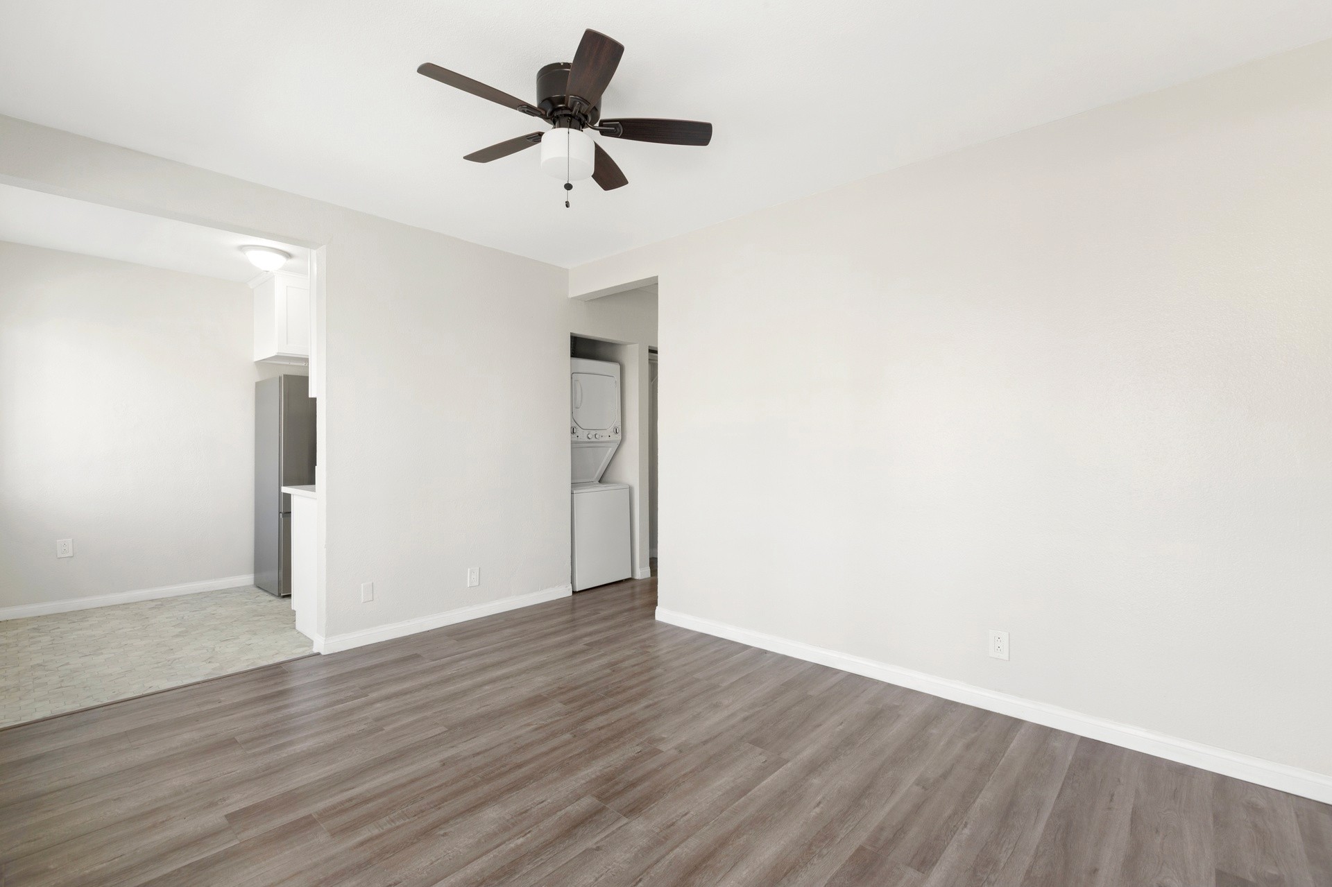 A bright, empty room at 4421 Wall, with a ceiling fan and dark wood-like flooring, featuring white walls and a door.