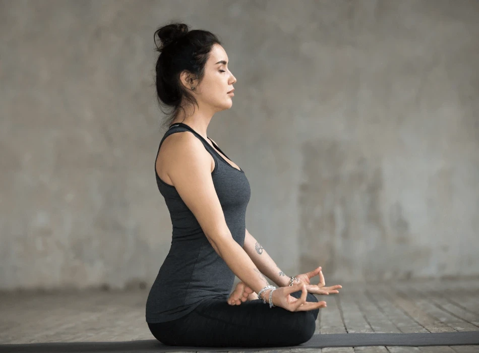 Woman meditating cross-legged on a yoga mat in a sunlit room, illustrating lifestyle support for PCOS.