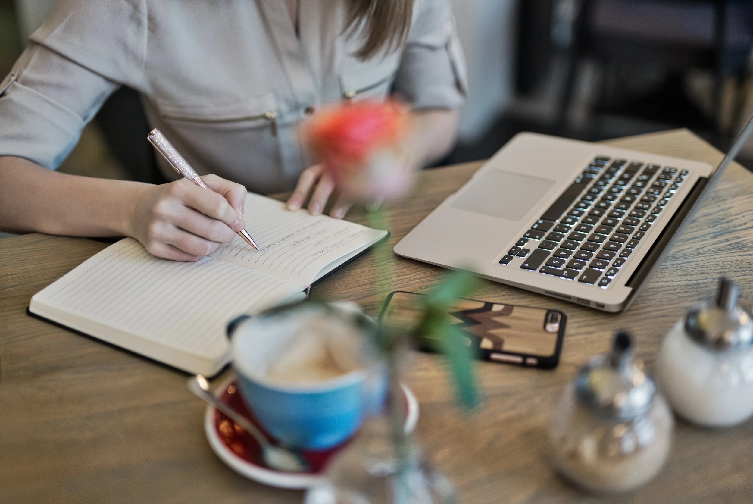 A person writing in a notebook beside a laptop and coffee, representing strategic B2B content planning.