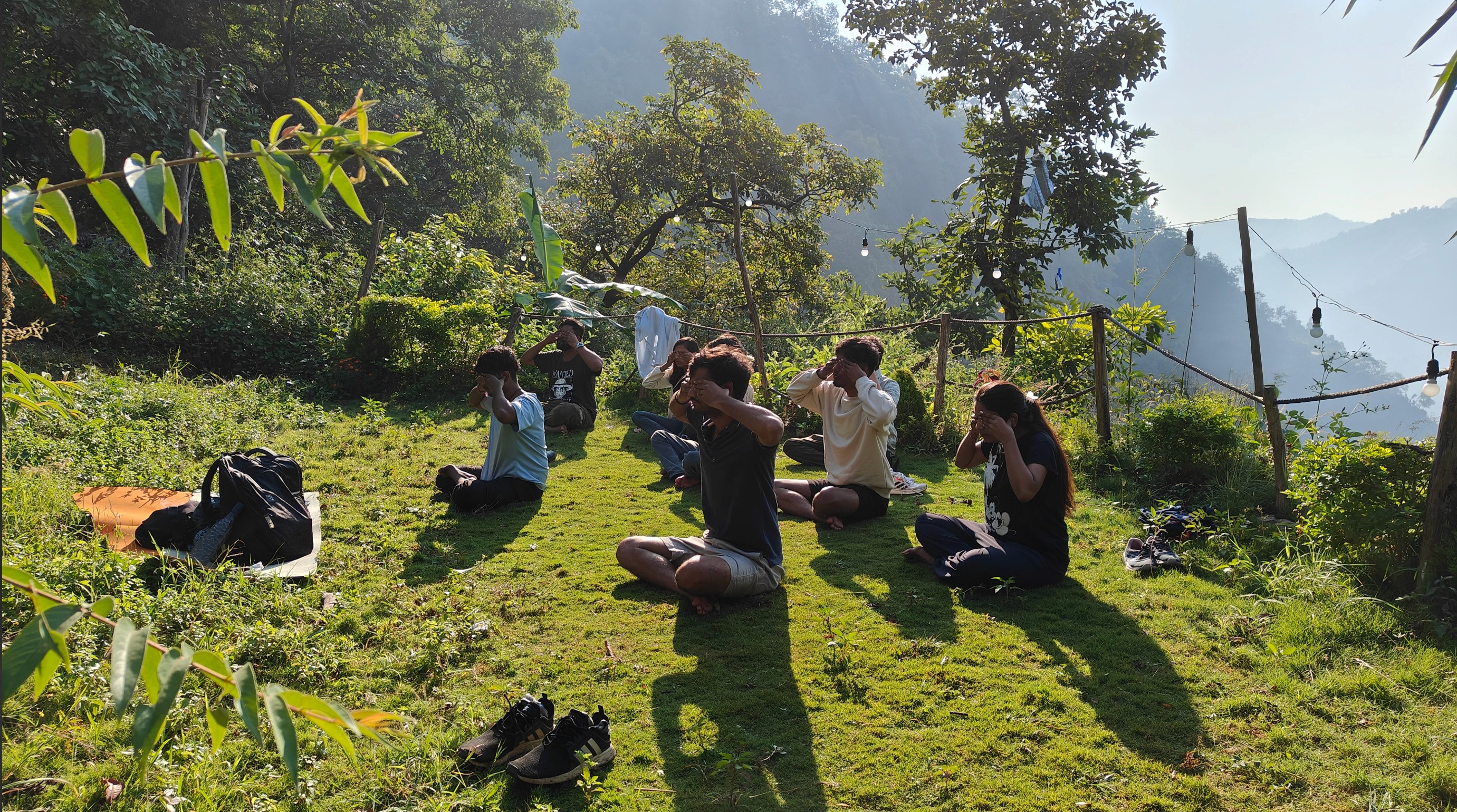 A group of people gathered on a grassy area, surrounded by trees and mountains under a clear sky doing Yoga, world yoga day, Team Wortham Rishikesh Trip 2024