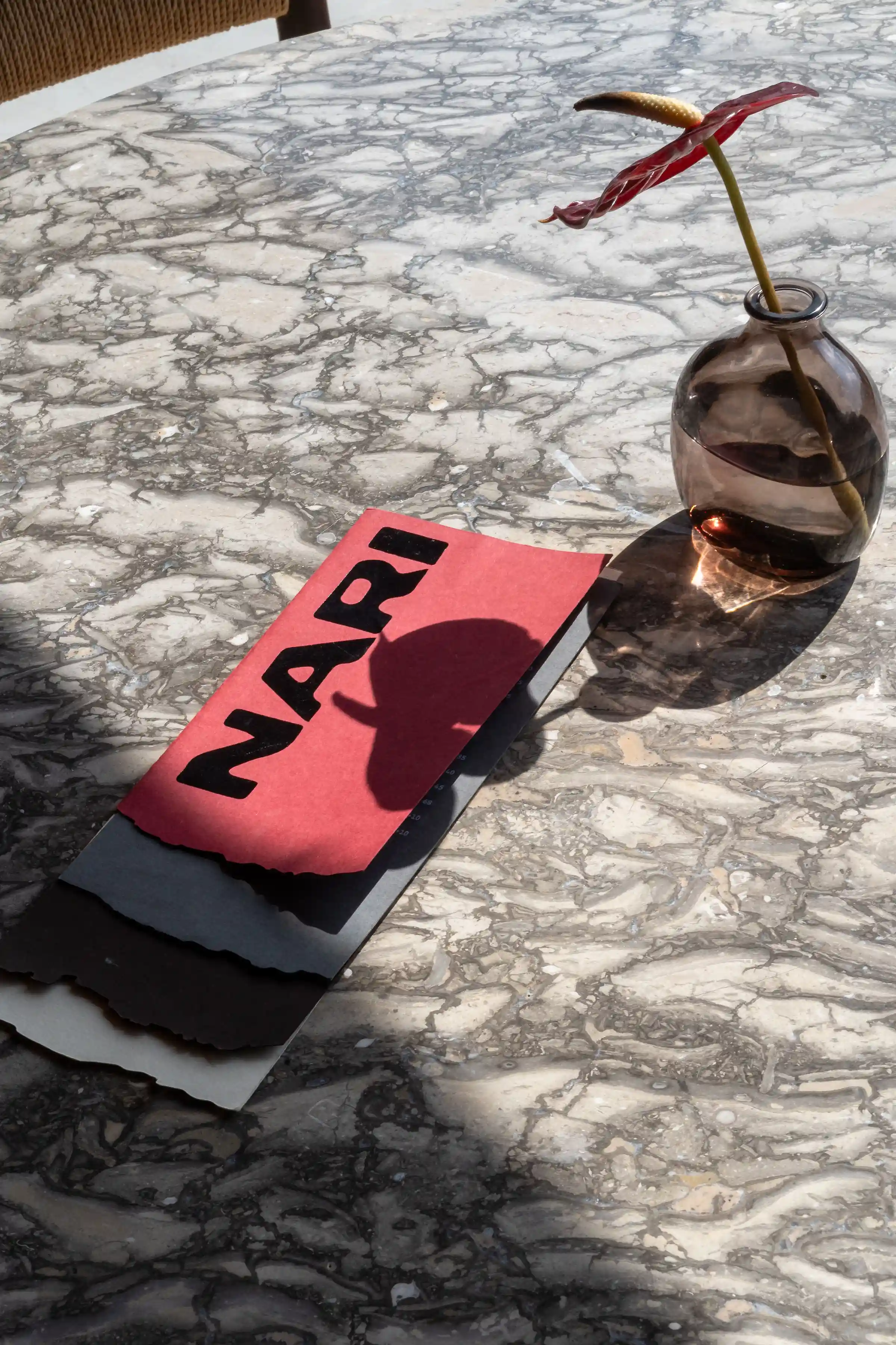 Nari Restaurant Ubud menu on marble table with flower vase in natural sunlight.