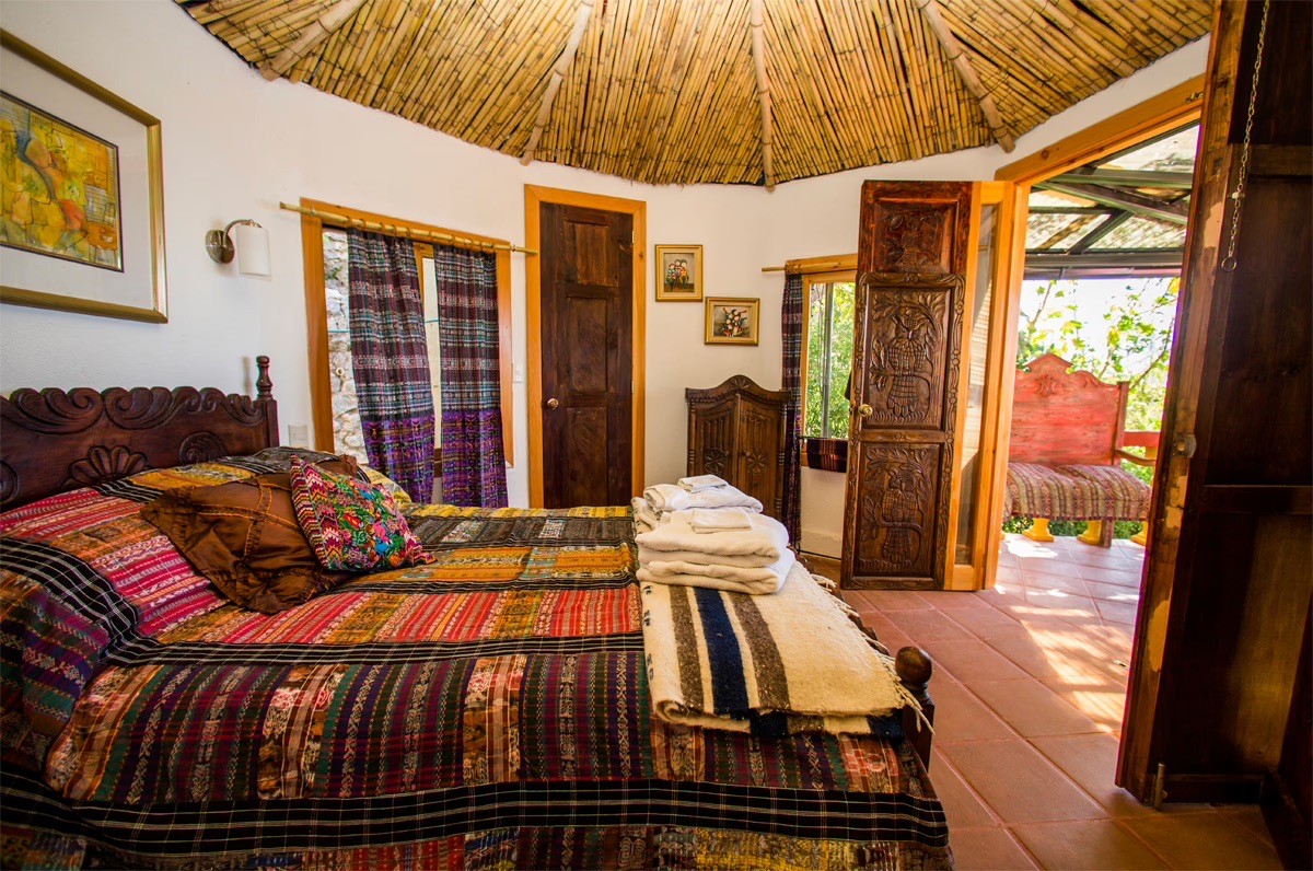 A bedroom with a thatched bamboo ceiling and a bed covered in a colorful, traditional woven textile spread.
