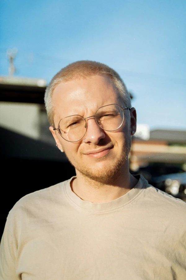 headshot of a young blond man with glasses and a beard, photo taken outdoors
