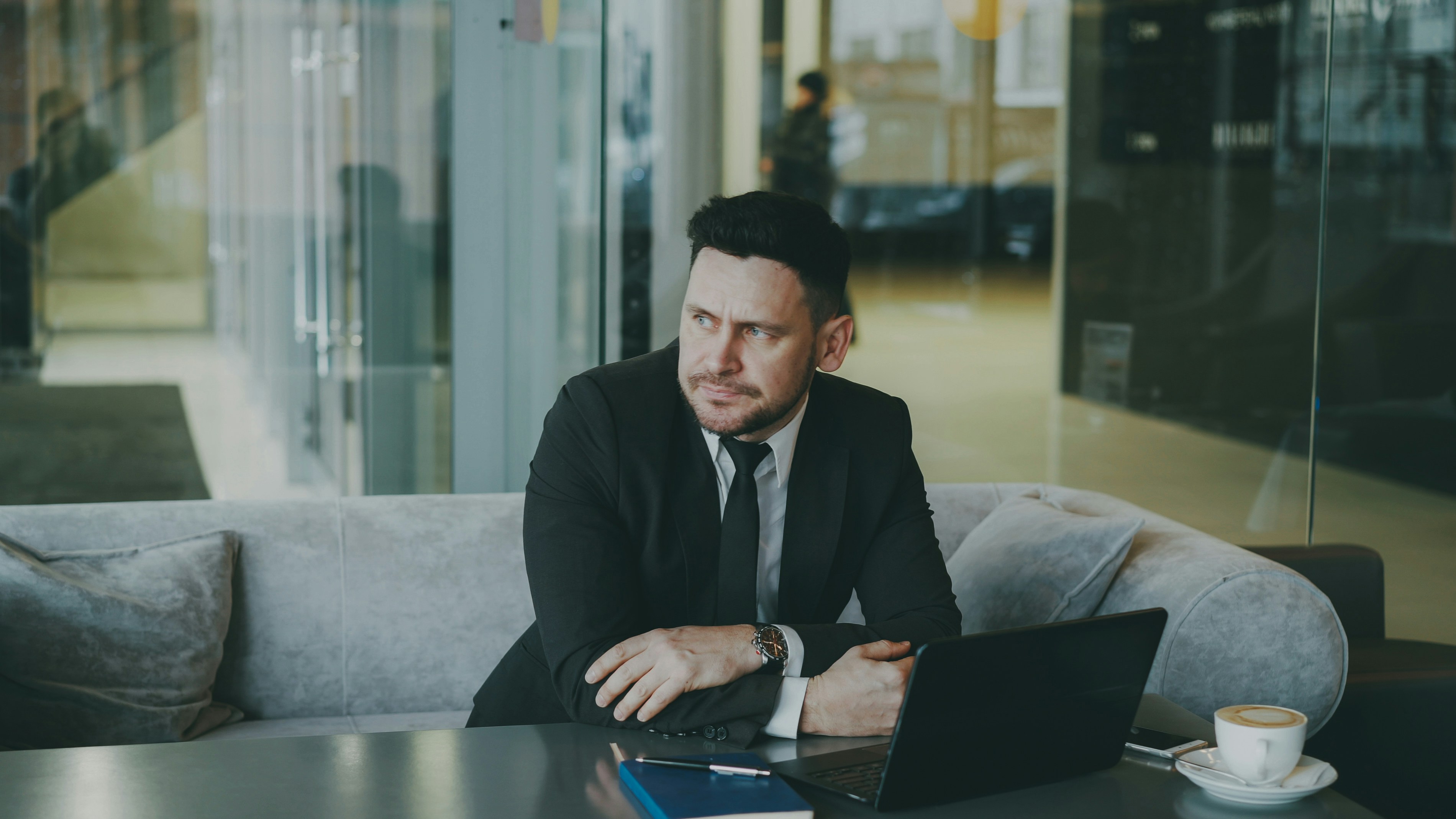Man in suit sitting at table with laptop and coffee.