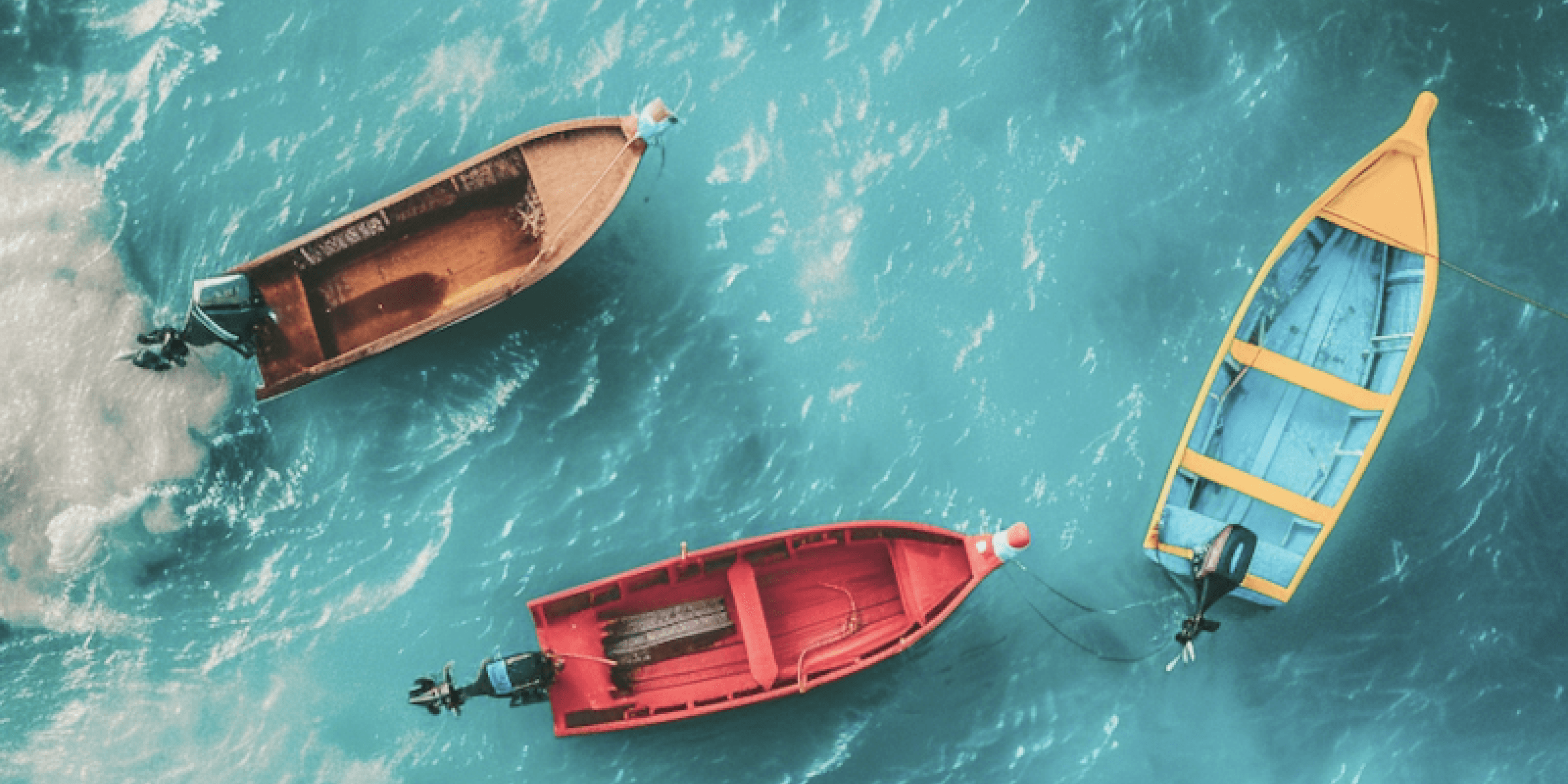 Three colorful boats floating on bright turquoise water seen from above.
