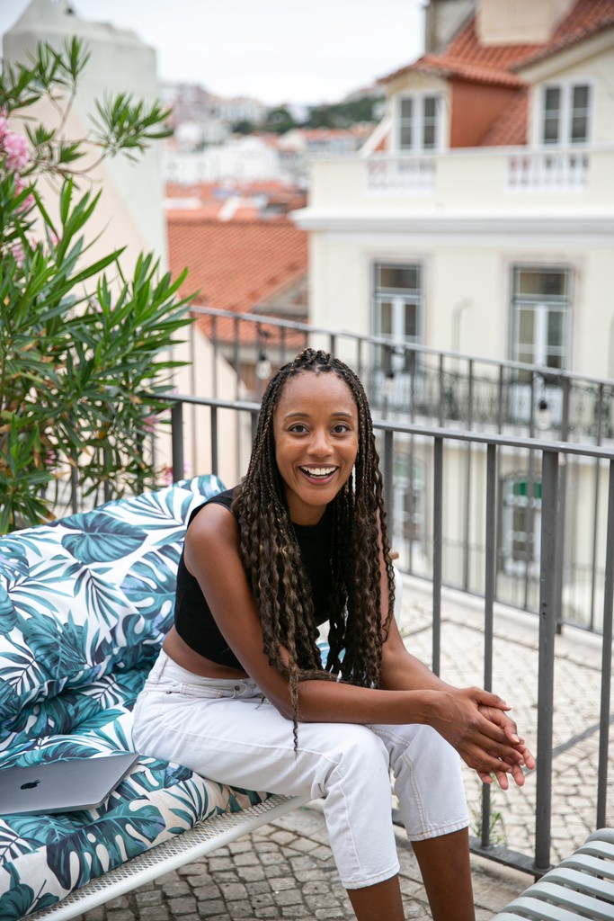 rita batalha sitting on a couch on an outdoor terrace smiling