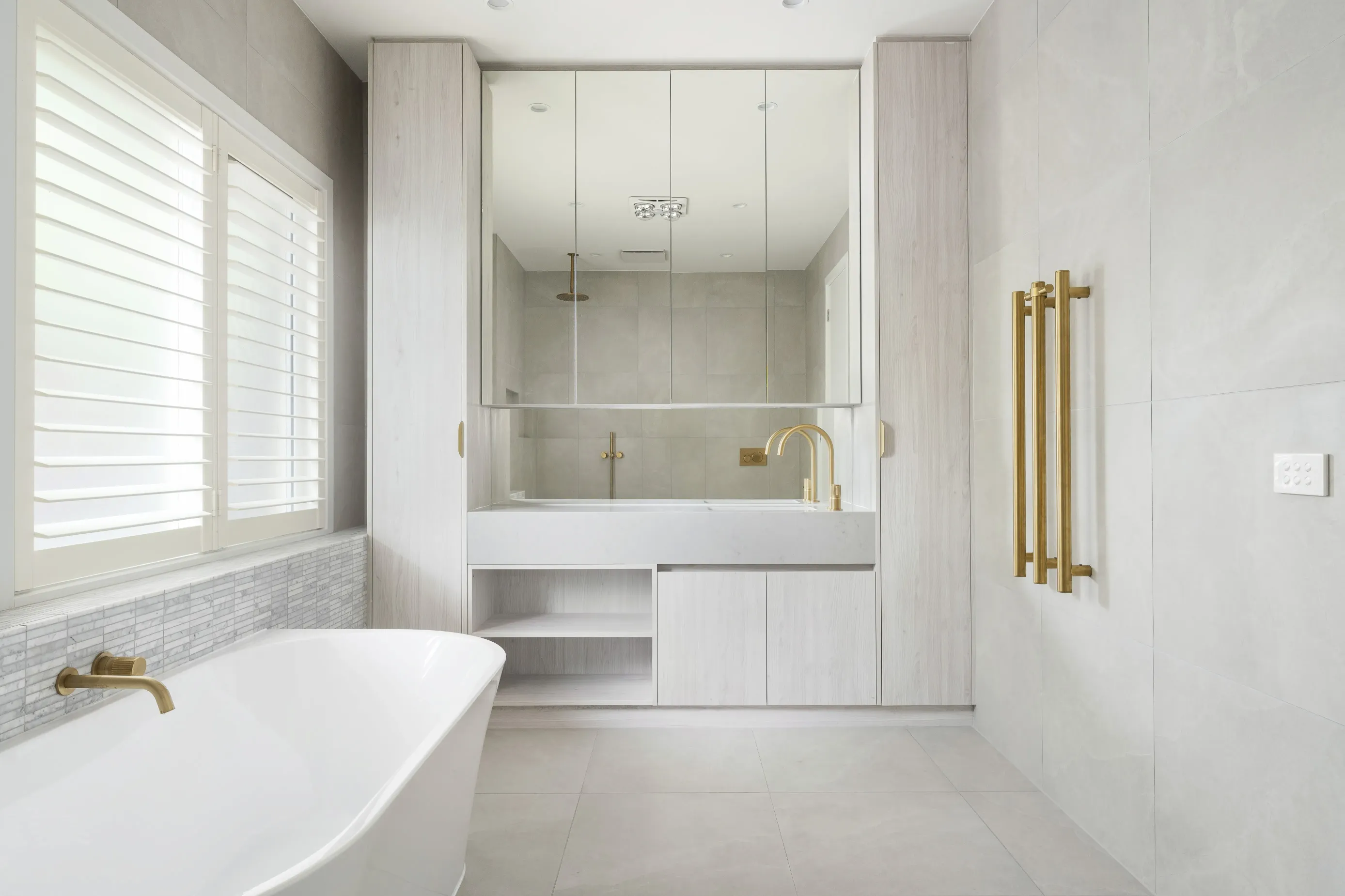 Bundoora bathroom with a freestanding white bath, plantation-shutter window, mirrored cabinetry and brushed-brass fittings