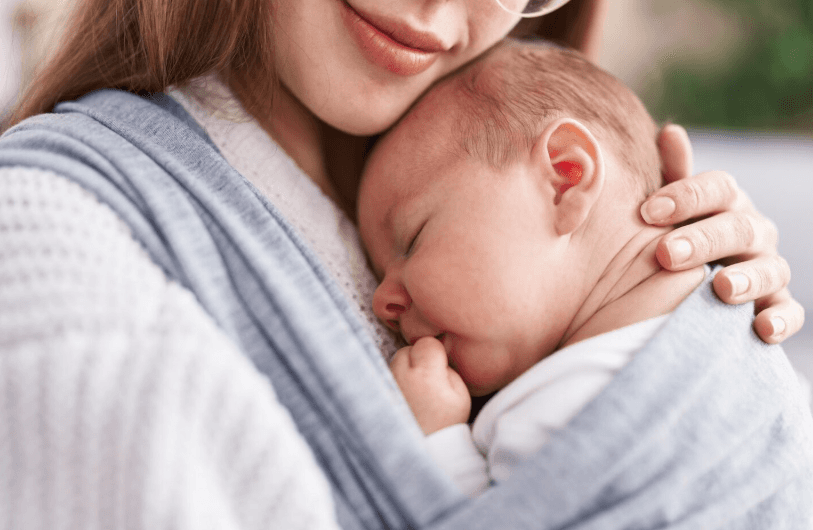 A mother cradles her newborn baby close to her chest, swaddled in blue fabric.