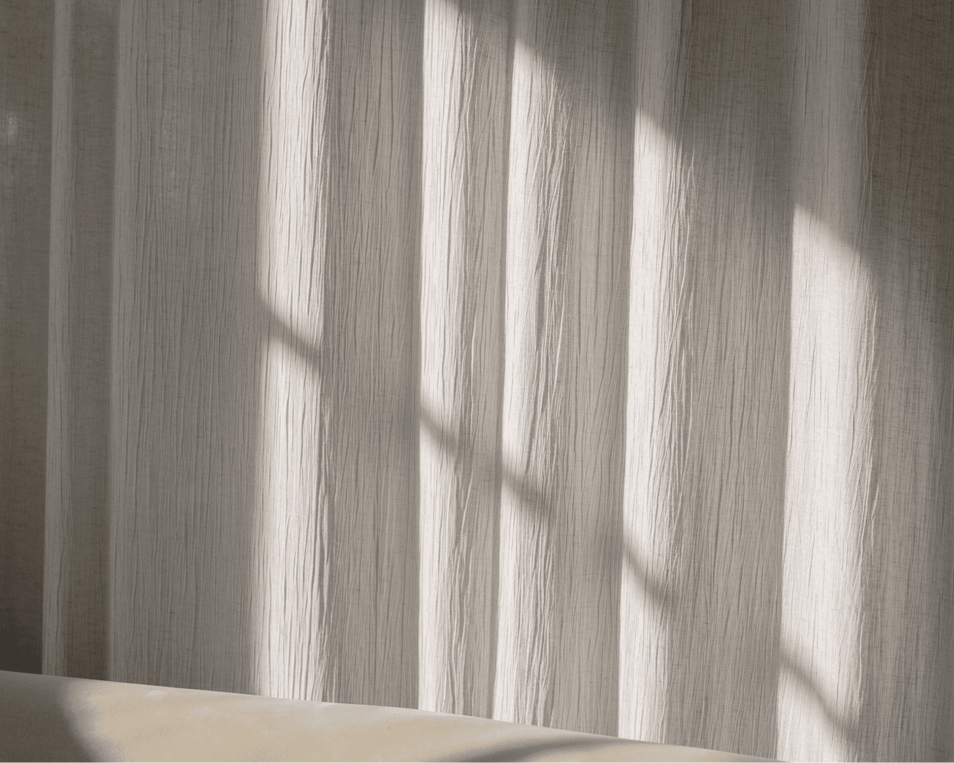Sunlight streams through a window, casting soft, diffused shadows on a beige fabric curtain.