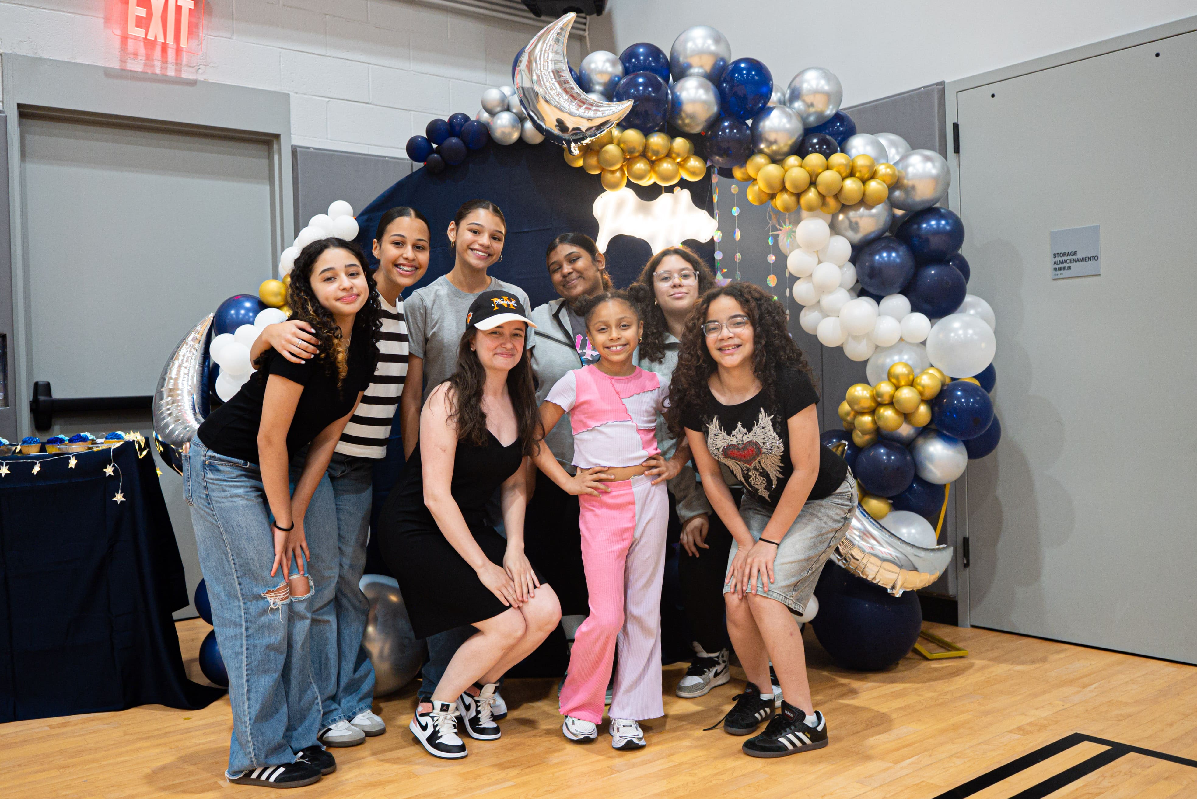 Young women pose in front of a balloon arch.