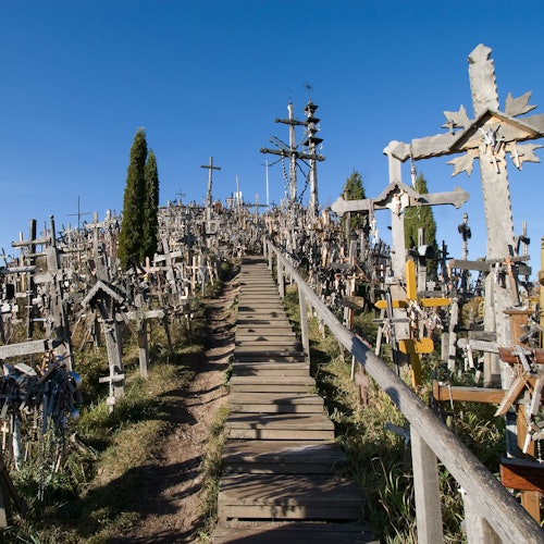 A hill covered with numerous crosses and a wooden path leading to the top under a clear blue sky.