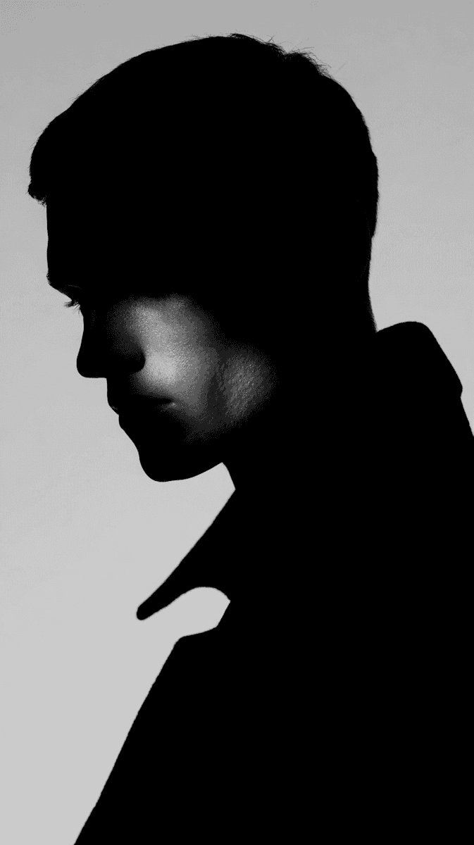Silhouette profile of a person looking down against a neutral gray background.