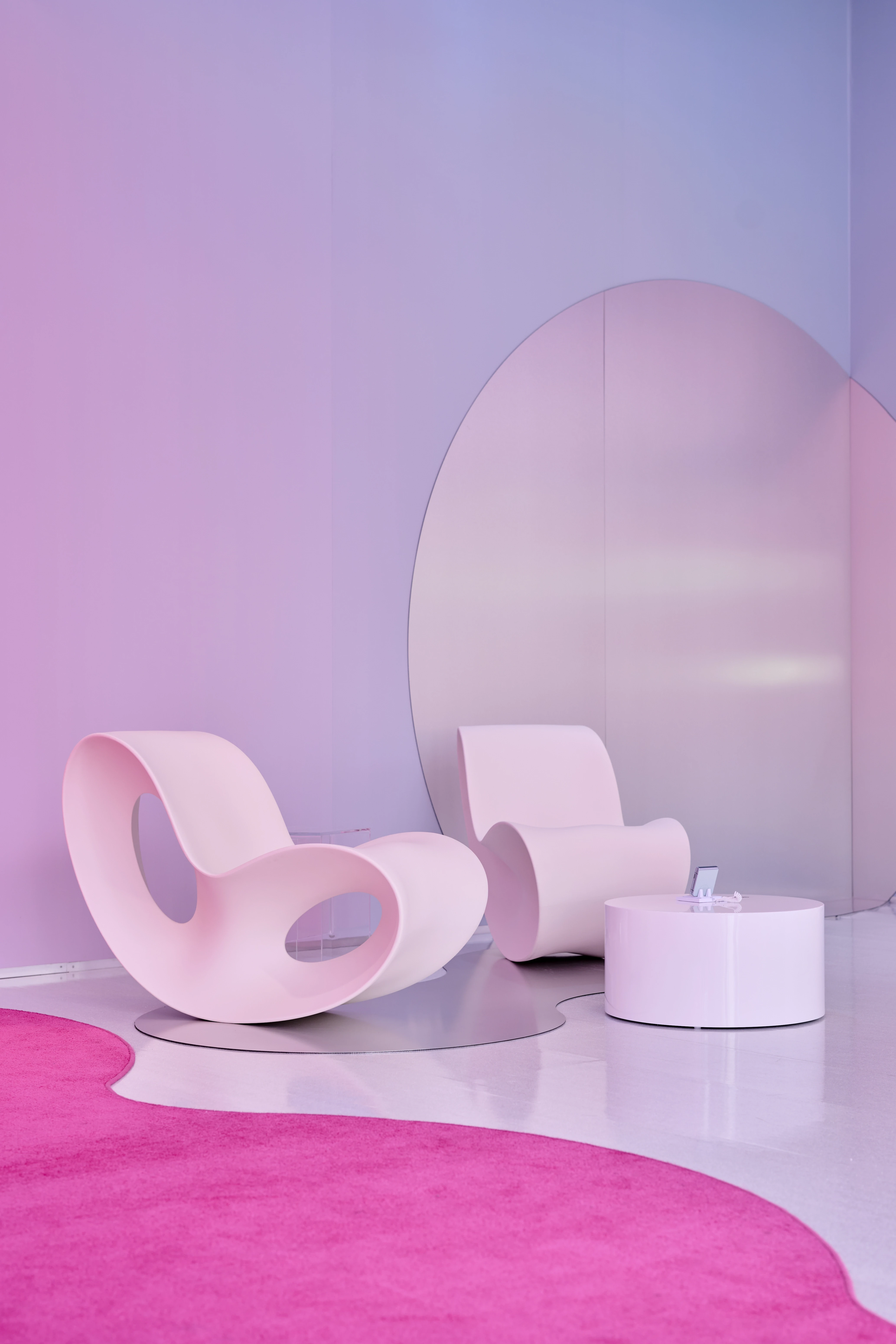 Pink Voido rocking chairs and round table in front of a circular metal mirror wall in the pastel lounge of the Samsung pop-up.