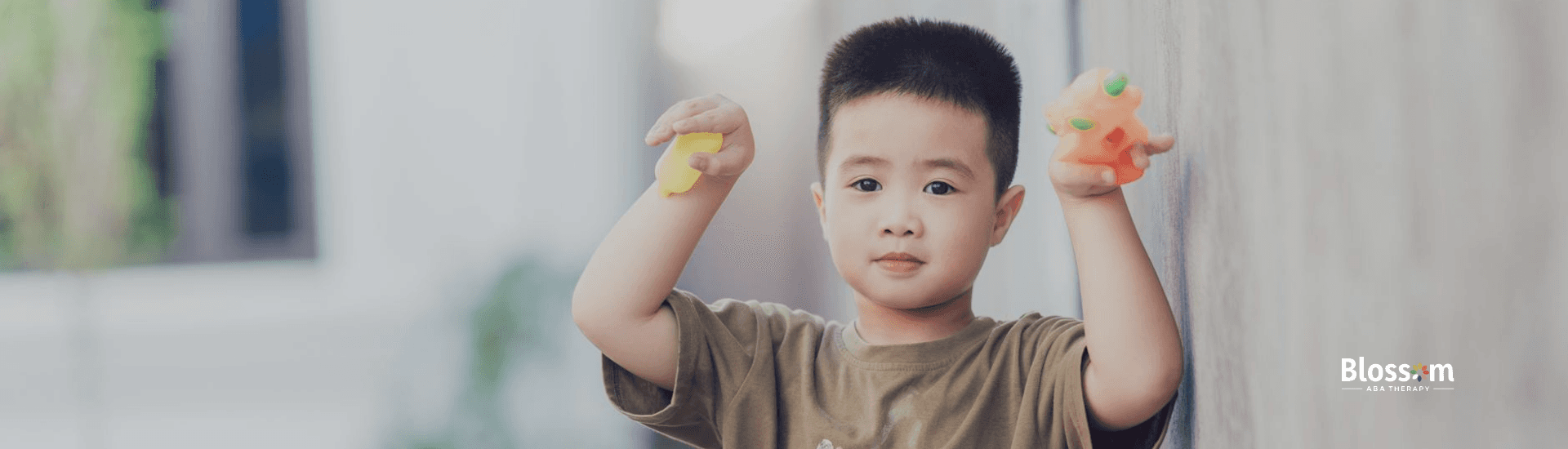 An autistic boy standing outside the streets of Maryland holding two toys, leaning against a wall.