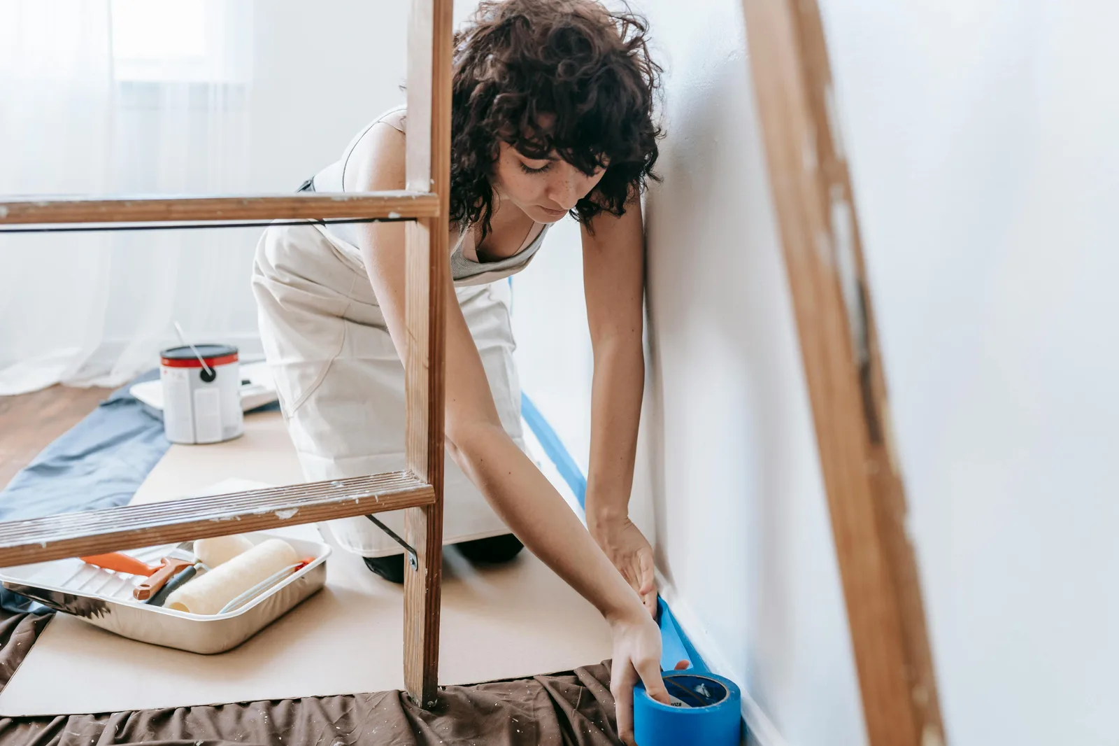 Woman applying blue painter tape along wall baseboard