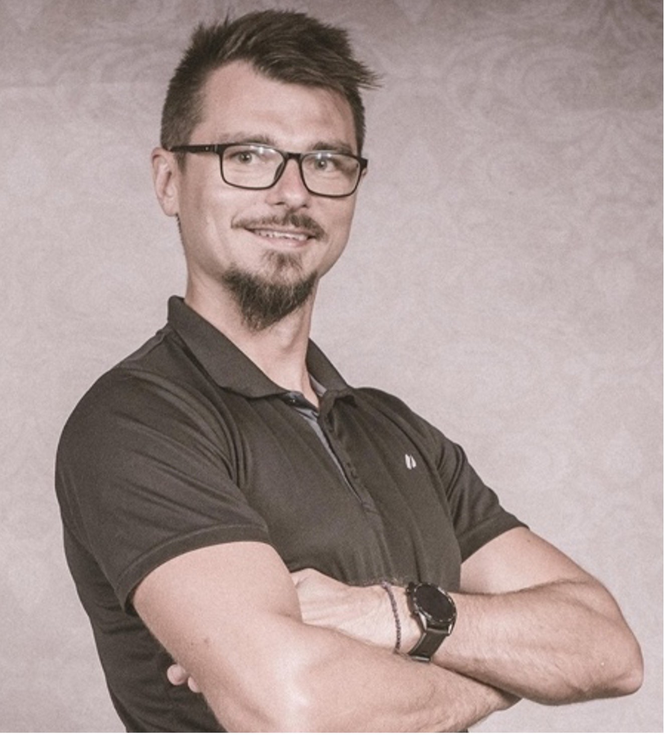 Zdjęcie przedstawia kobietę o jasnych, falowanych włosach i okularach w ciemnych oprawkach. Ma na sobie czarną bluzkę z wzorem i patrzy prosto w obiektyw. Tło jest jednolite, ciemne.