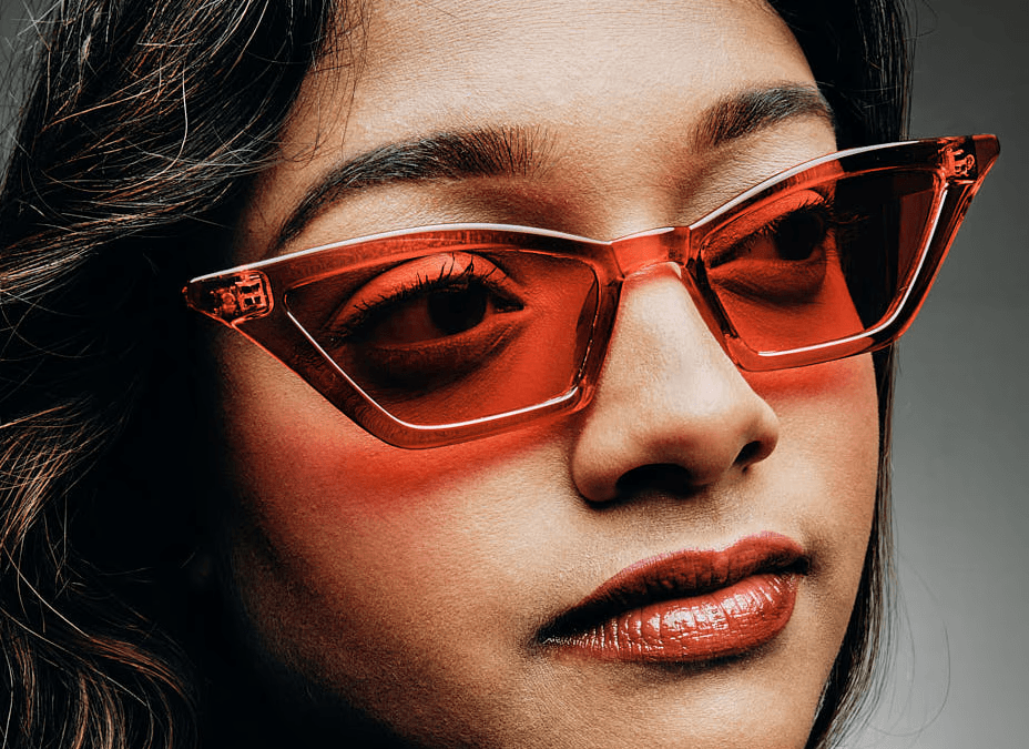 A close-up of a person wearing green-tinted glasses, with a serious expression and smooth skin.