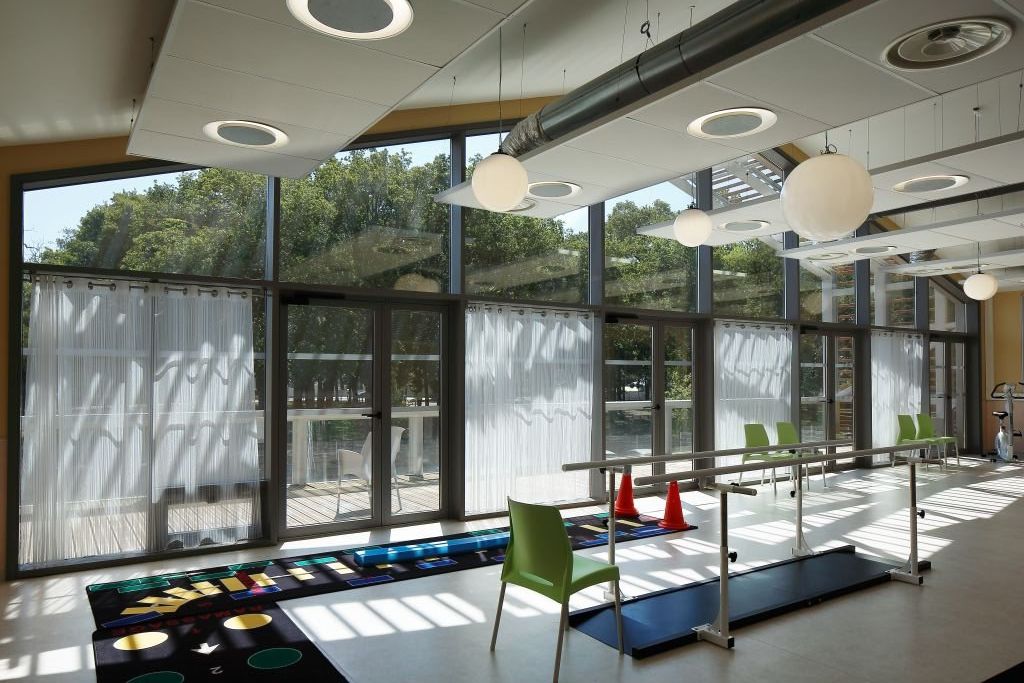 Physical therapy room with exercise equipment	parallel bars	and rehabilitation facilities with natural light through large windows