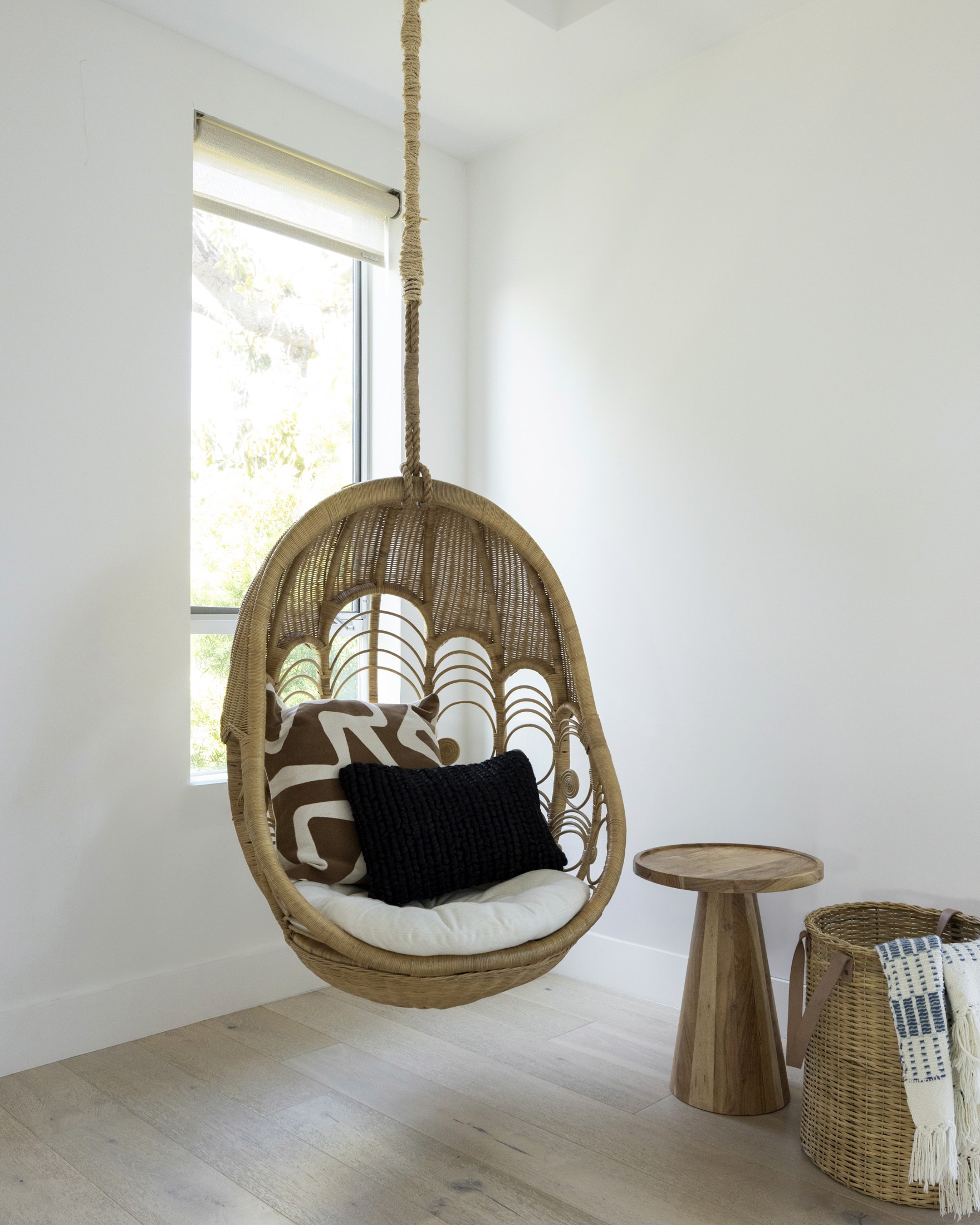 Hanging accent chair in corner of living room with wood accent table and woven basket