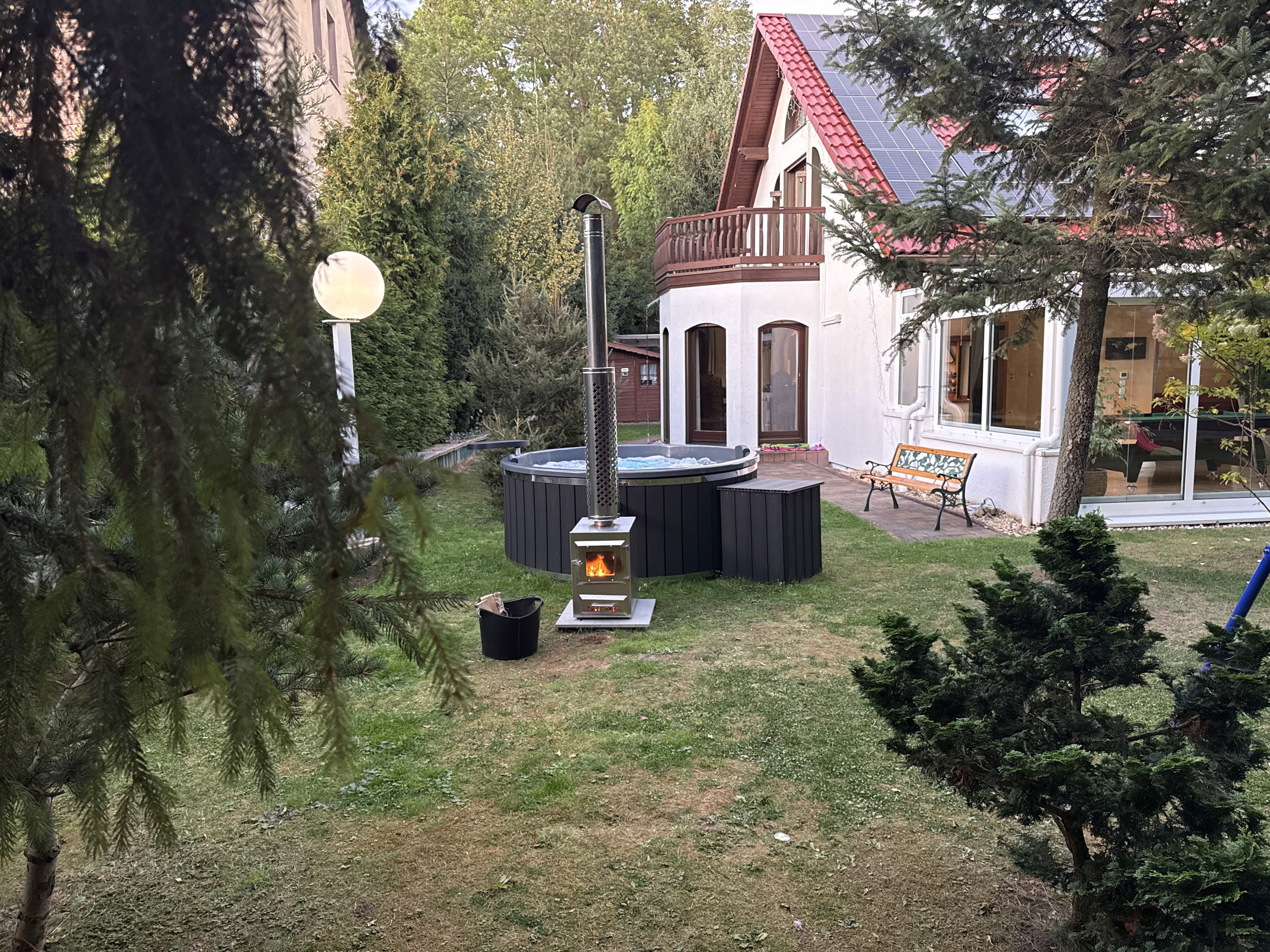 Outdoor hot tub installation with wood-fired heater in a backyard near a modern house