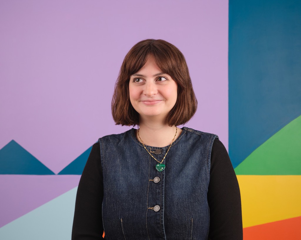 Portrait of Rhiann Moore standing in front of a colourful mural