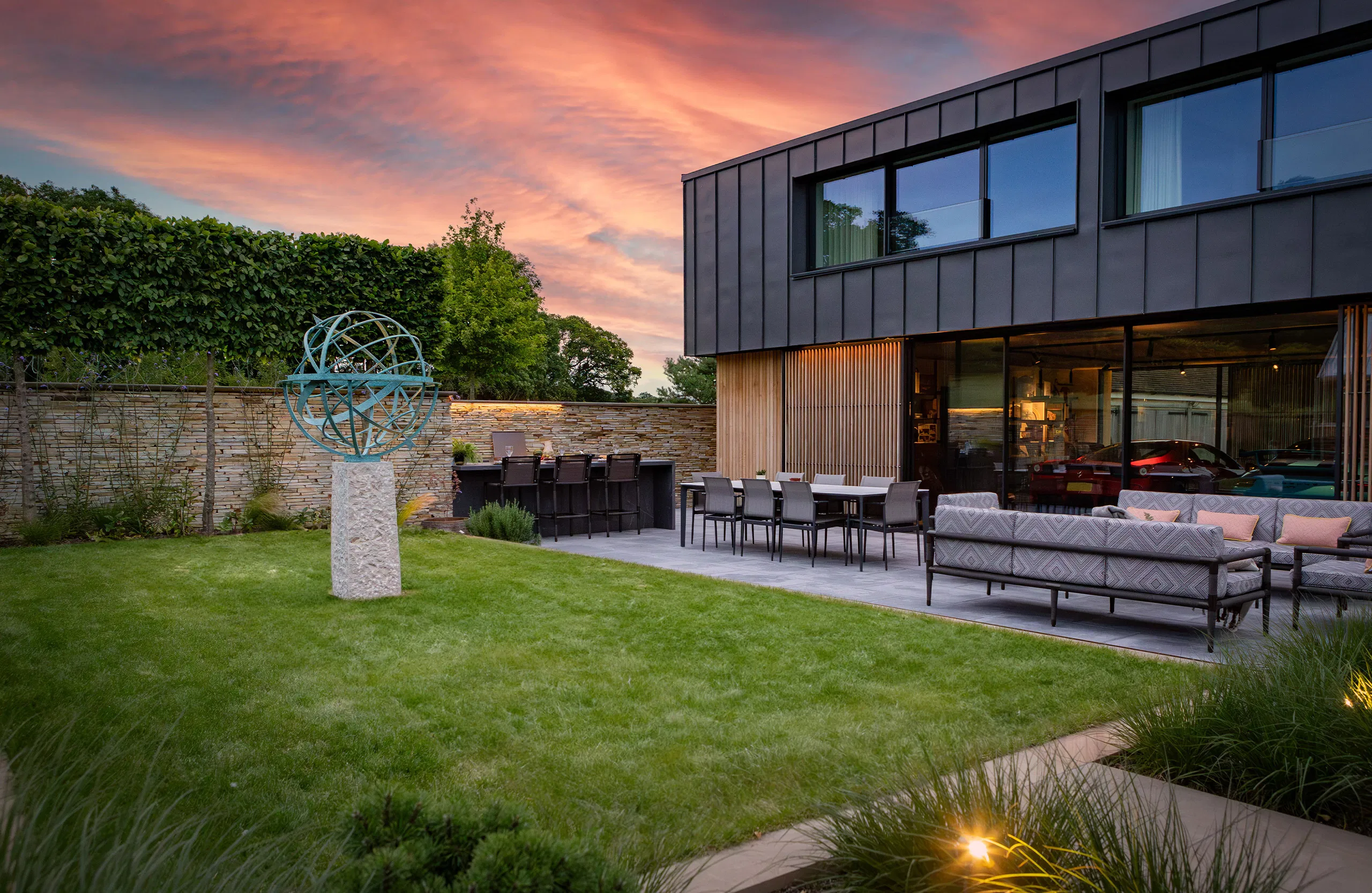 Modern home with a landscaped garden, seating area, and a sunset sky in the background.
