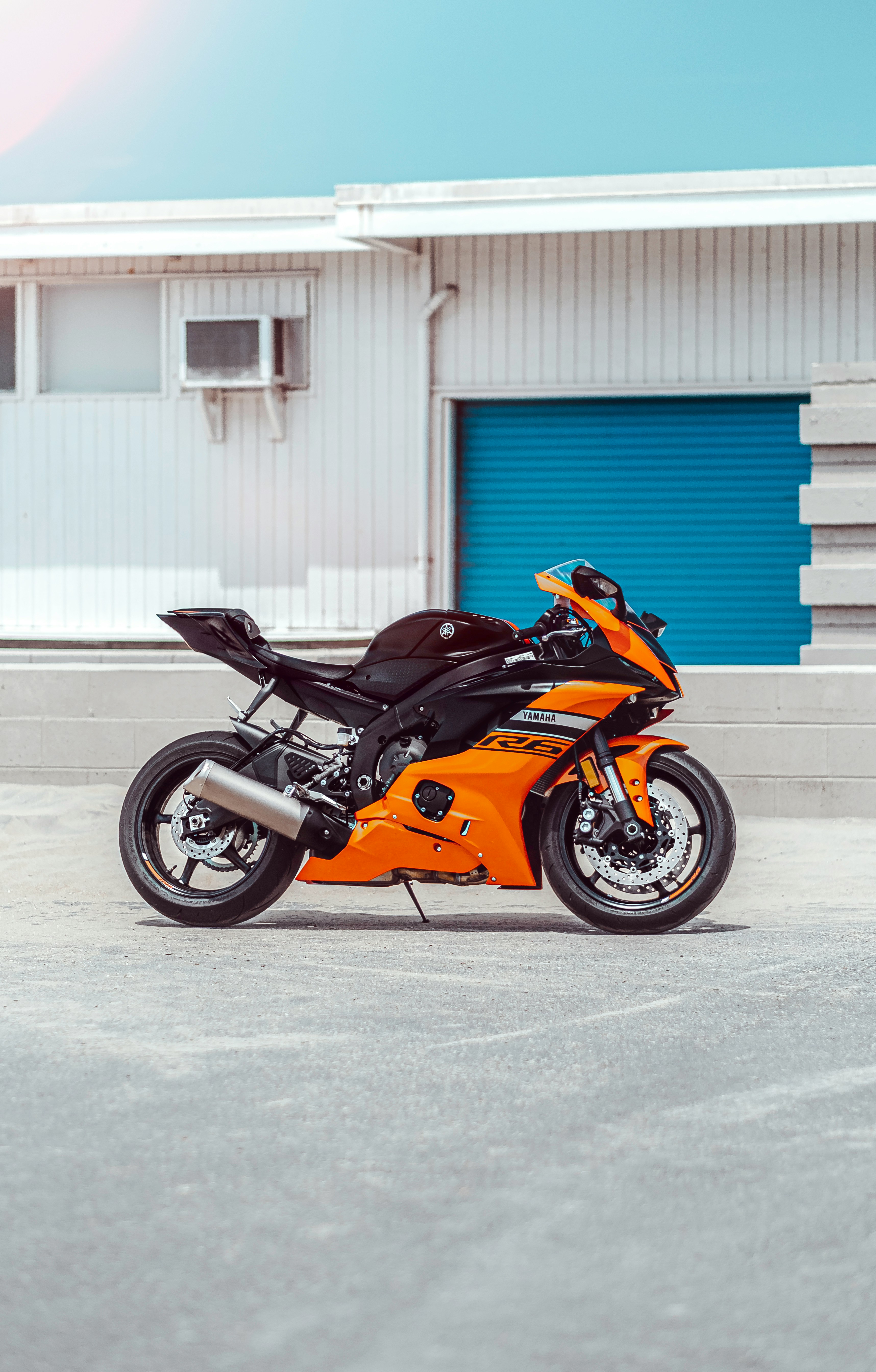 orange and black sports bike parked beside blue and white building